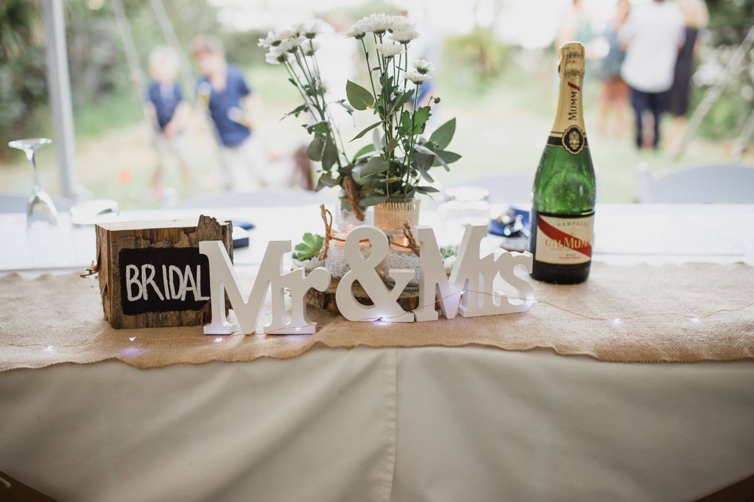 A table setting for a wedding with a bunch of white daisies and a bottle of wine