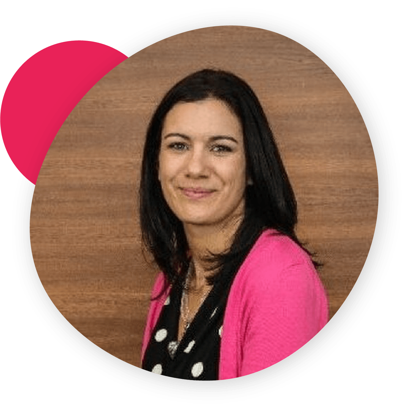 Smiling woman with dark hair wearing a pink cardigan and polka dot top, framed within a circular shape with a pink accent, against a wooden background