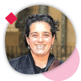 Portrait of a woman with short curly hair and facial tattoos, smiling, framed by a pink circle with geometric accents