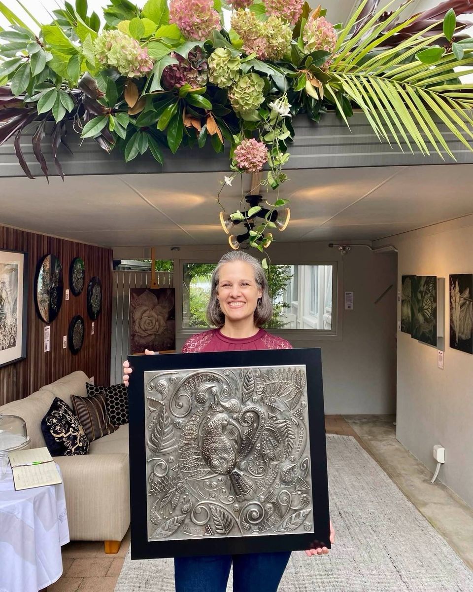 Ninette Kruger holding Huia's Lustrous Lacework, a 60 x 60cm pewter wall art piece, in a gallery