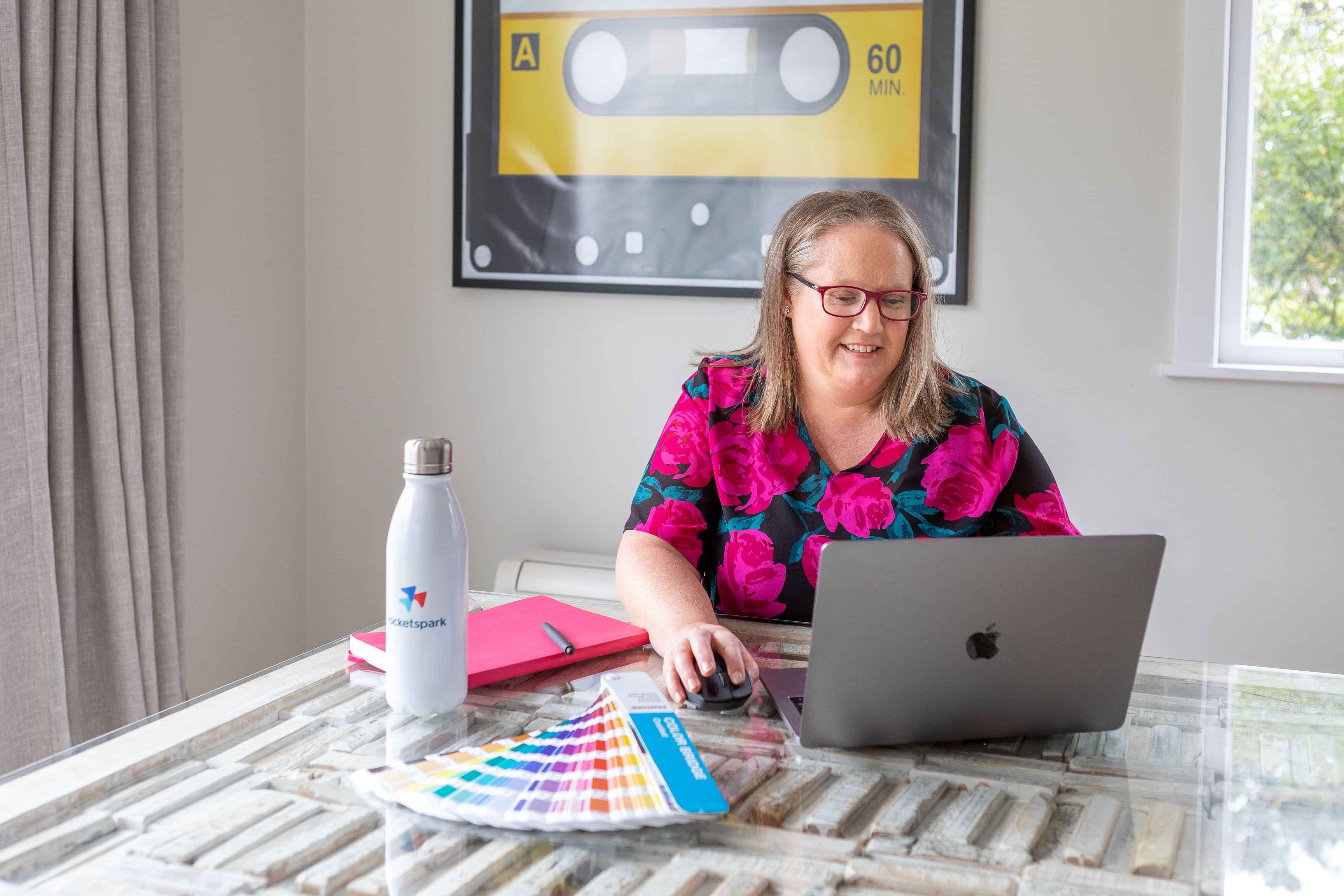Catherine working at a laptop with a colour guide  and notebook on the table