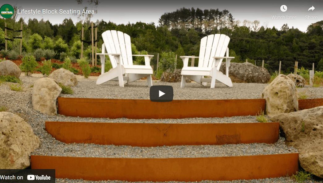 An informal outdoor seating rea at the top of a set of curved steps that have rust-look corten steel risers, and a rounded pebble fill. Sitting at the