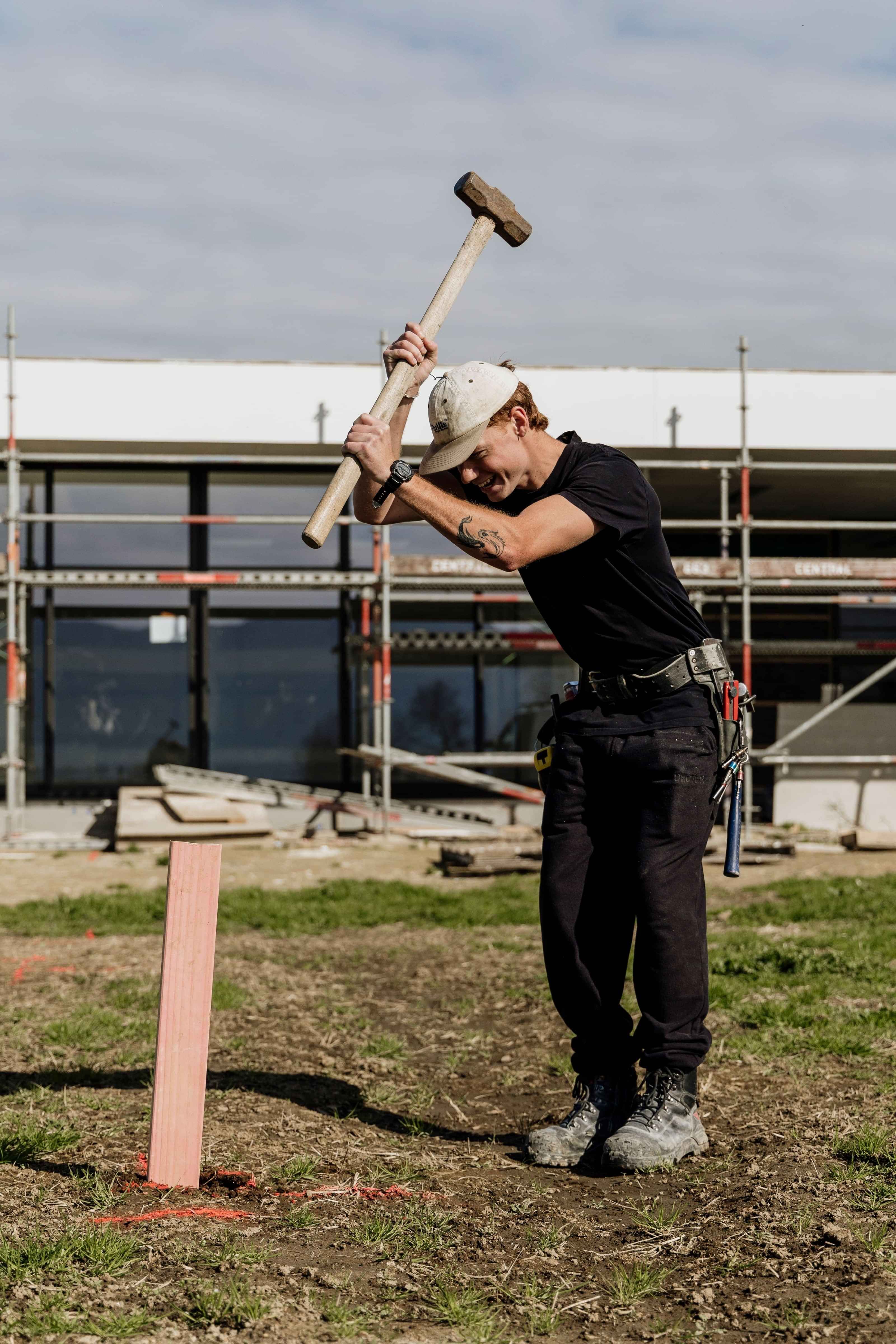 Linecrest builder bangs in a peg using a sledgehammer, marking out the pool area on a rural unique high-end build in Waharoa.