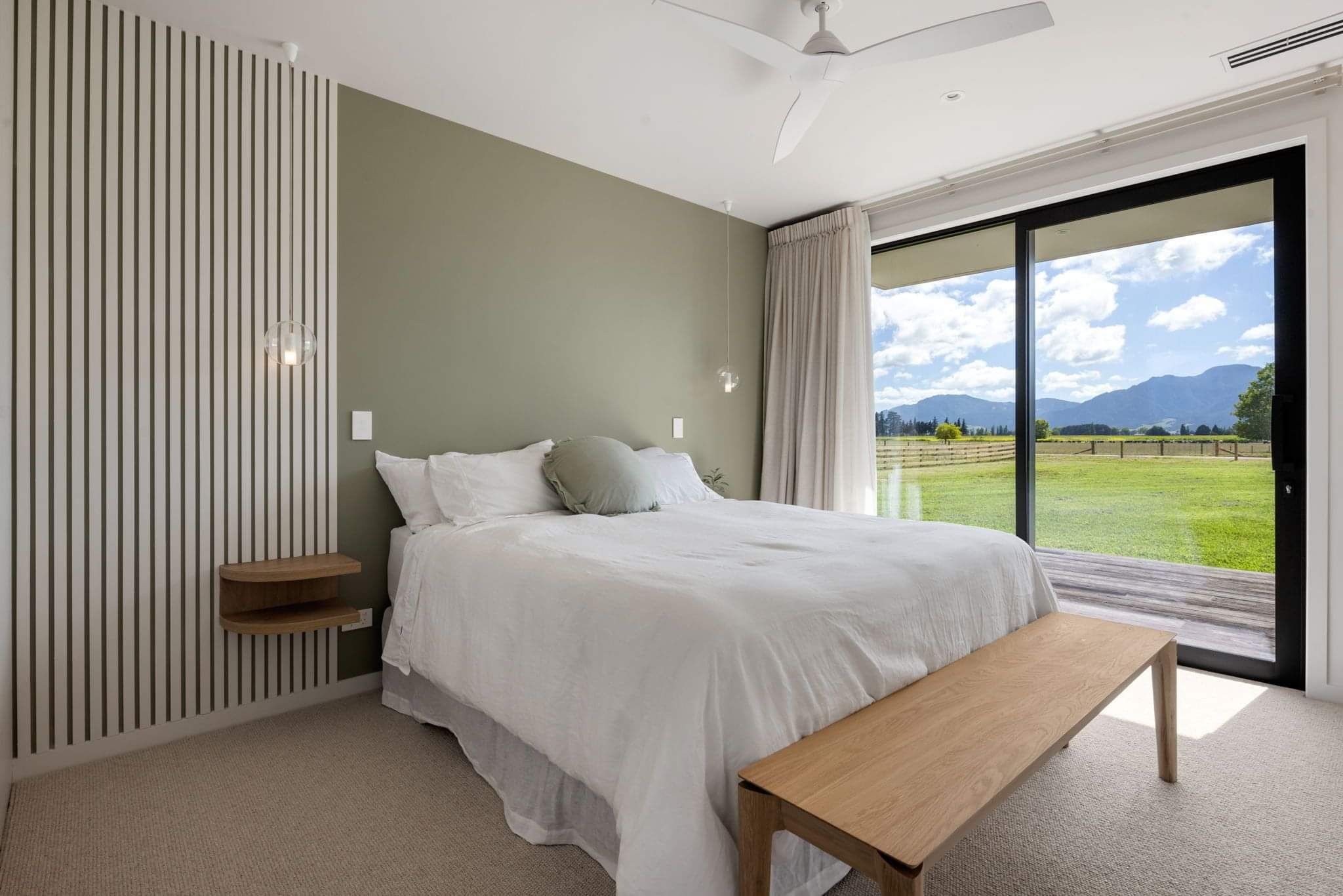 A minimalist design for the master bedroom features full-height glass doors leading to a deck that overlooks rural views.