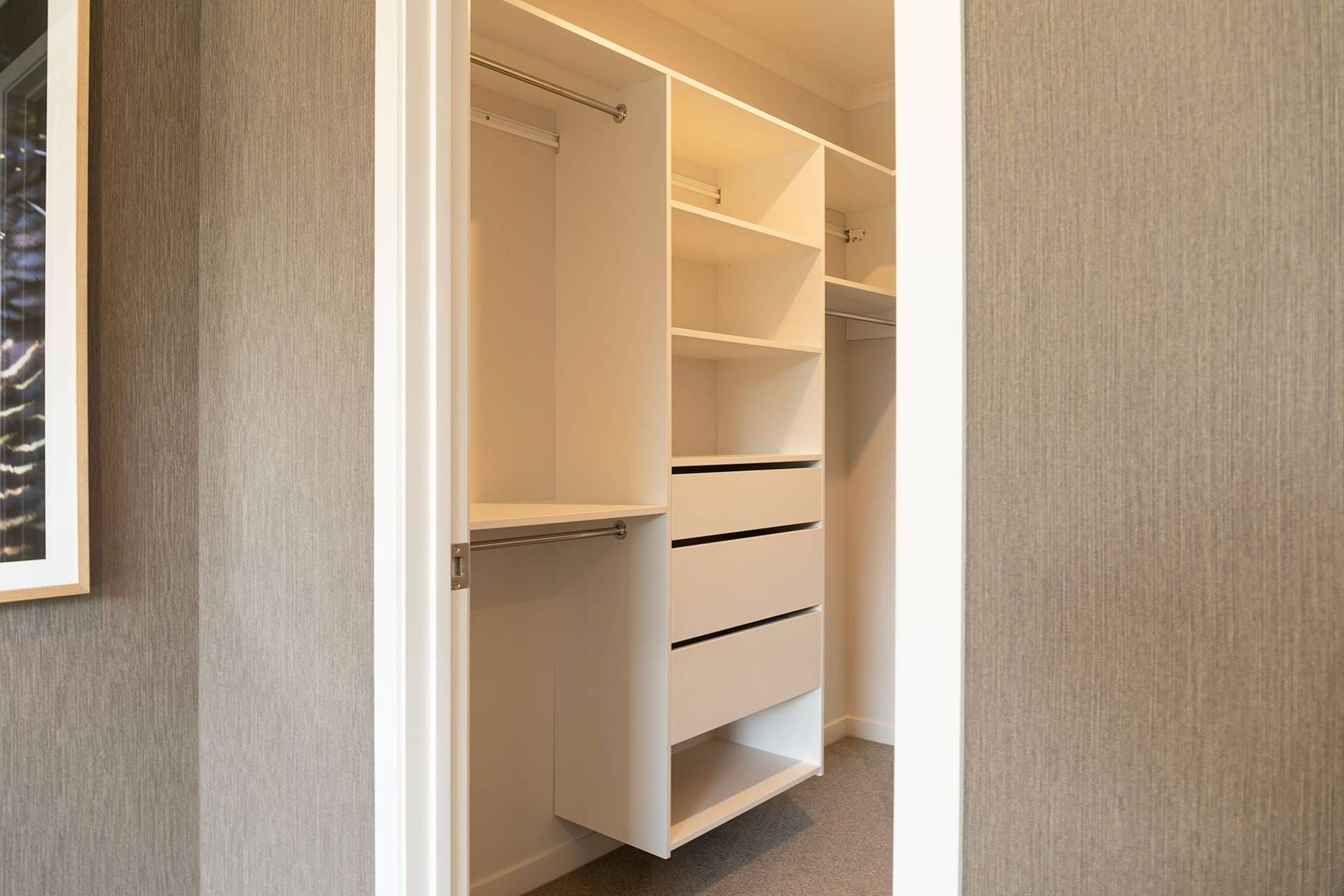 Looking through a door way from the bedroom into the custom walk-in-closet, showing the Victoria Wardrobe System. 