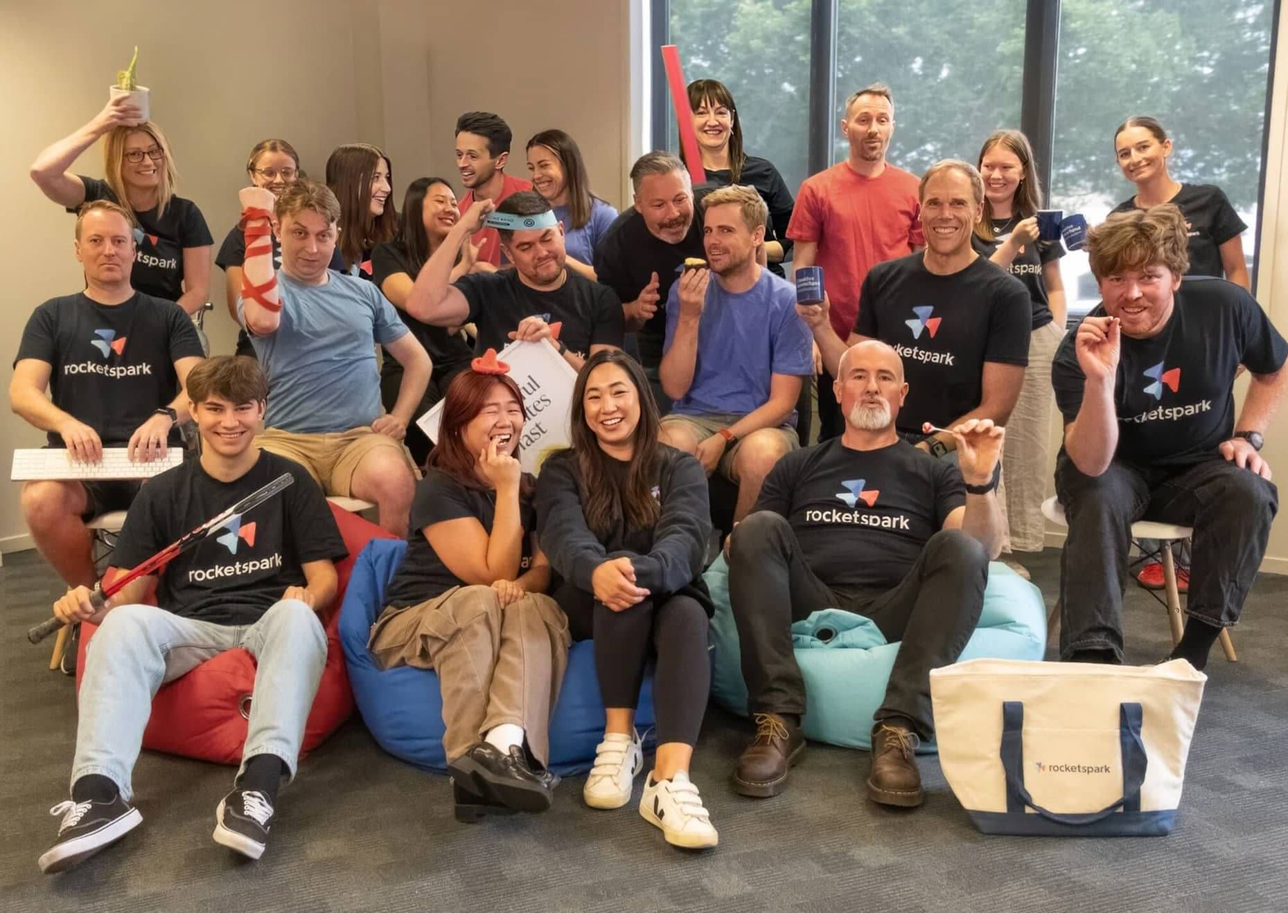 The Rocketspark team in branded t-shirts laughing together in the Cambridge office, holding a "Beautiful websites fast" poster