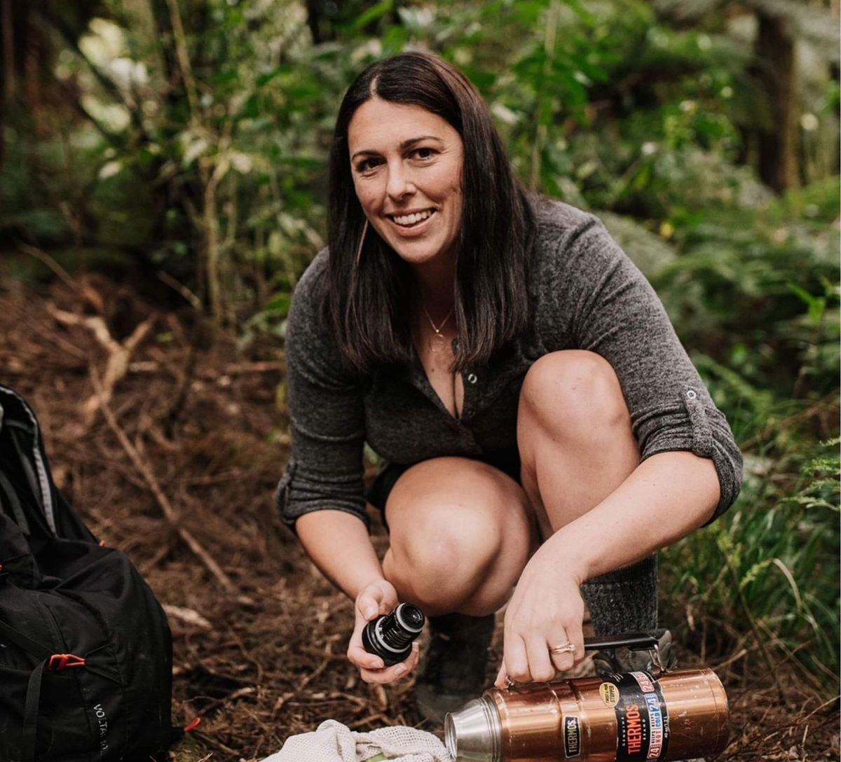 Kylie from The Bush Boardroom pouring a drink from a thermos in native bush