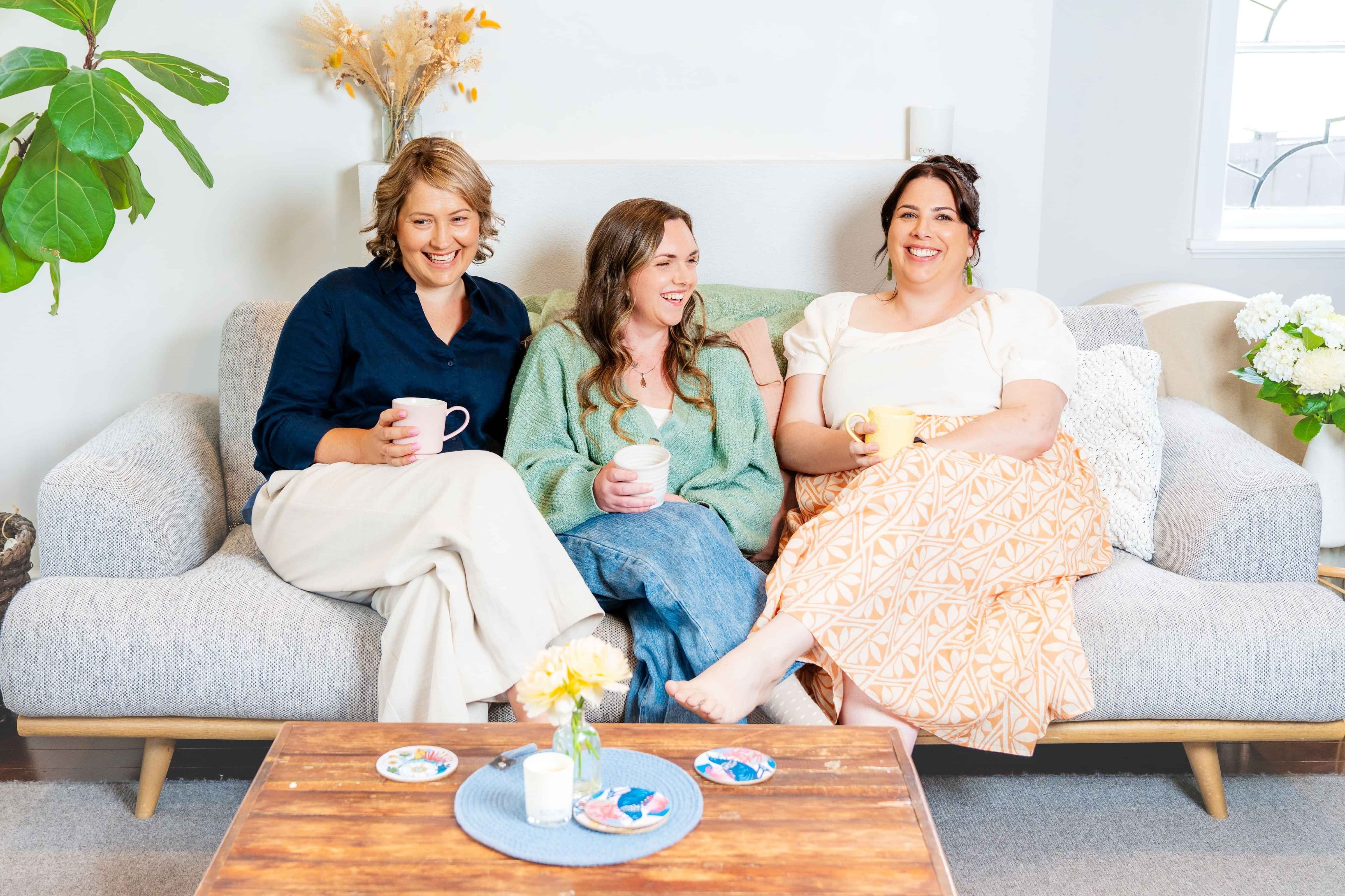 Directors of Aotearoa Diabetes Collective Rachael, Solita and Claire sitting on a couch holding cups of tea and laughing