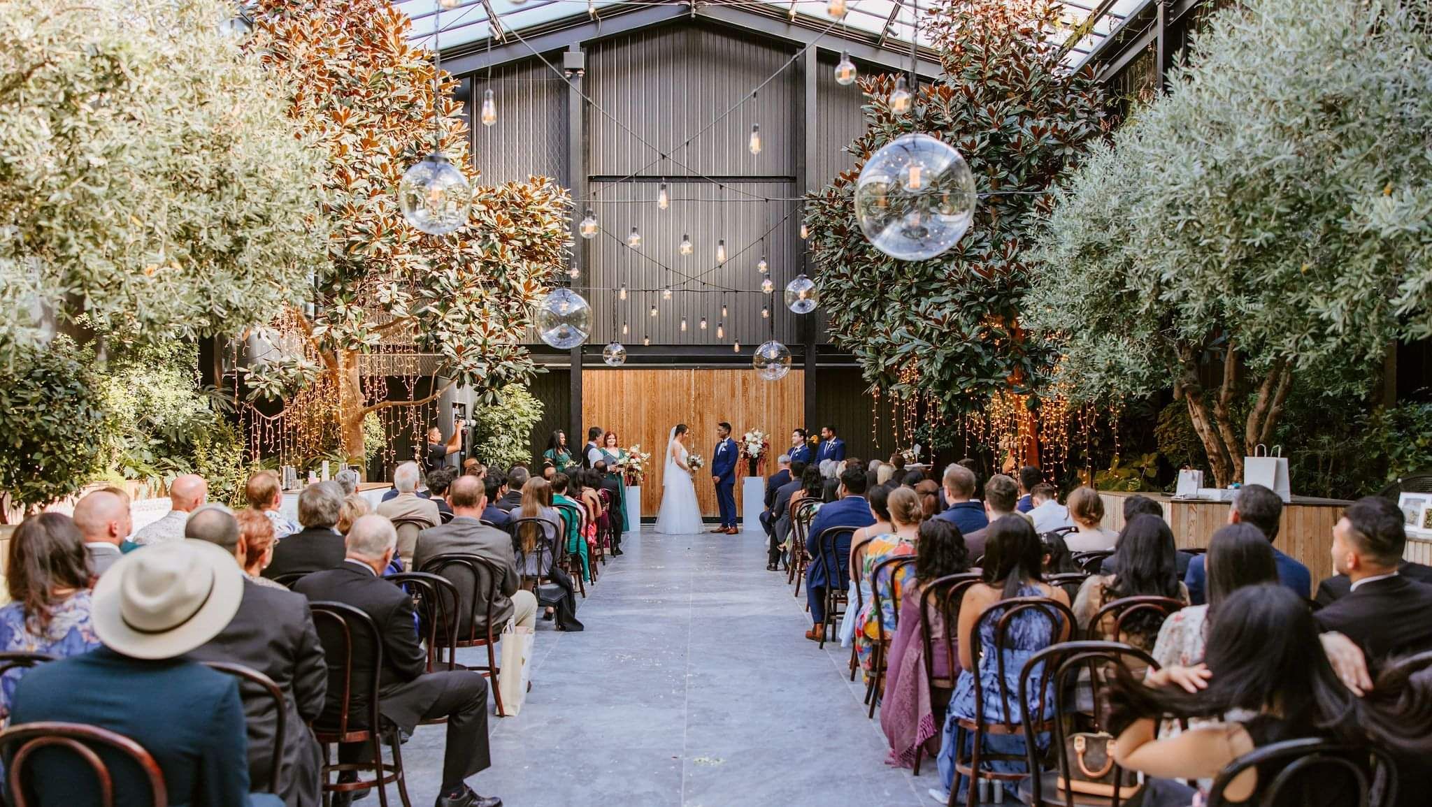 Mark Trubuhovich officiating a couple's wedding ceremony in an indoor greenhouse venue