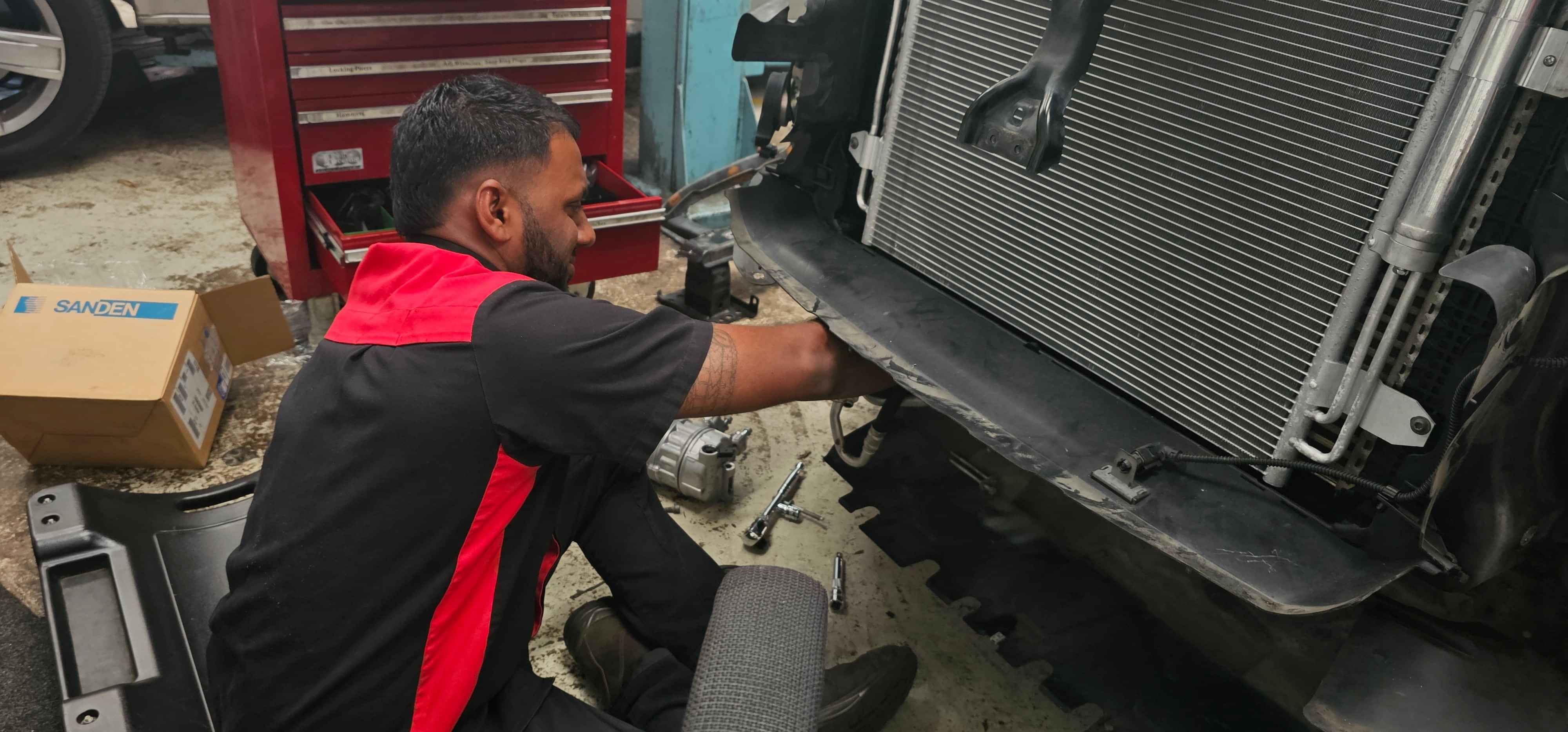 Side profile of CoolCar Henderson Workshop Manager, Navneel, smiling while remocing condenser from truck