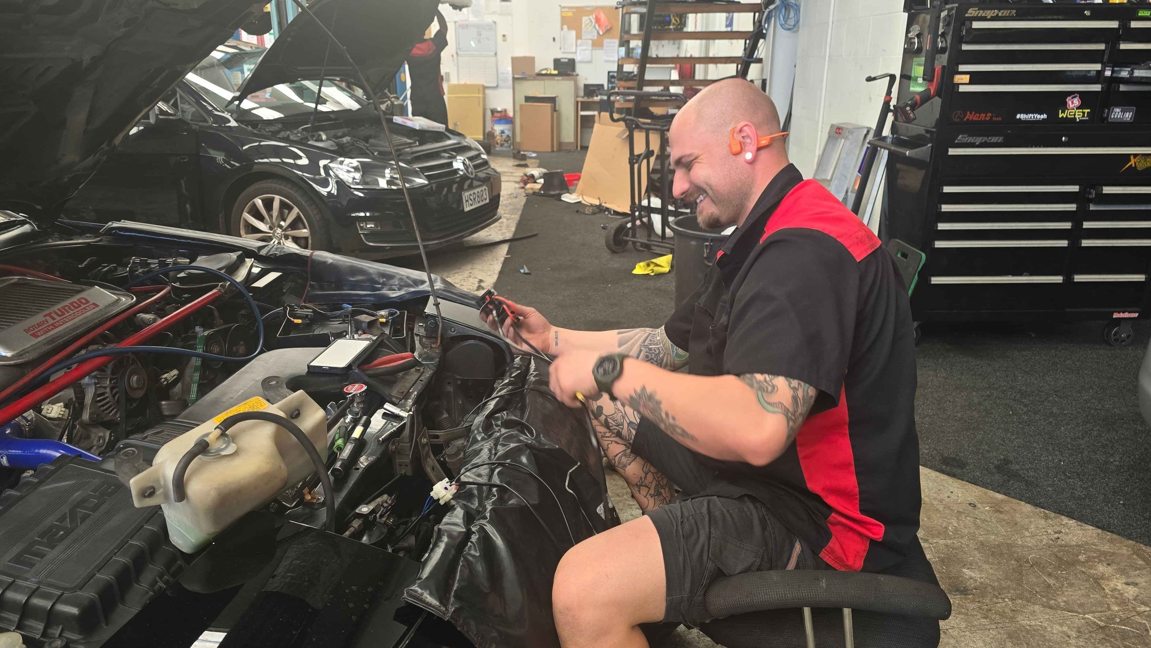 Branch Manager, Alex Daniels, smiling and working on electrics in customer's vehicle.