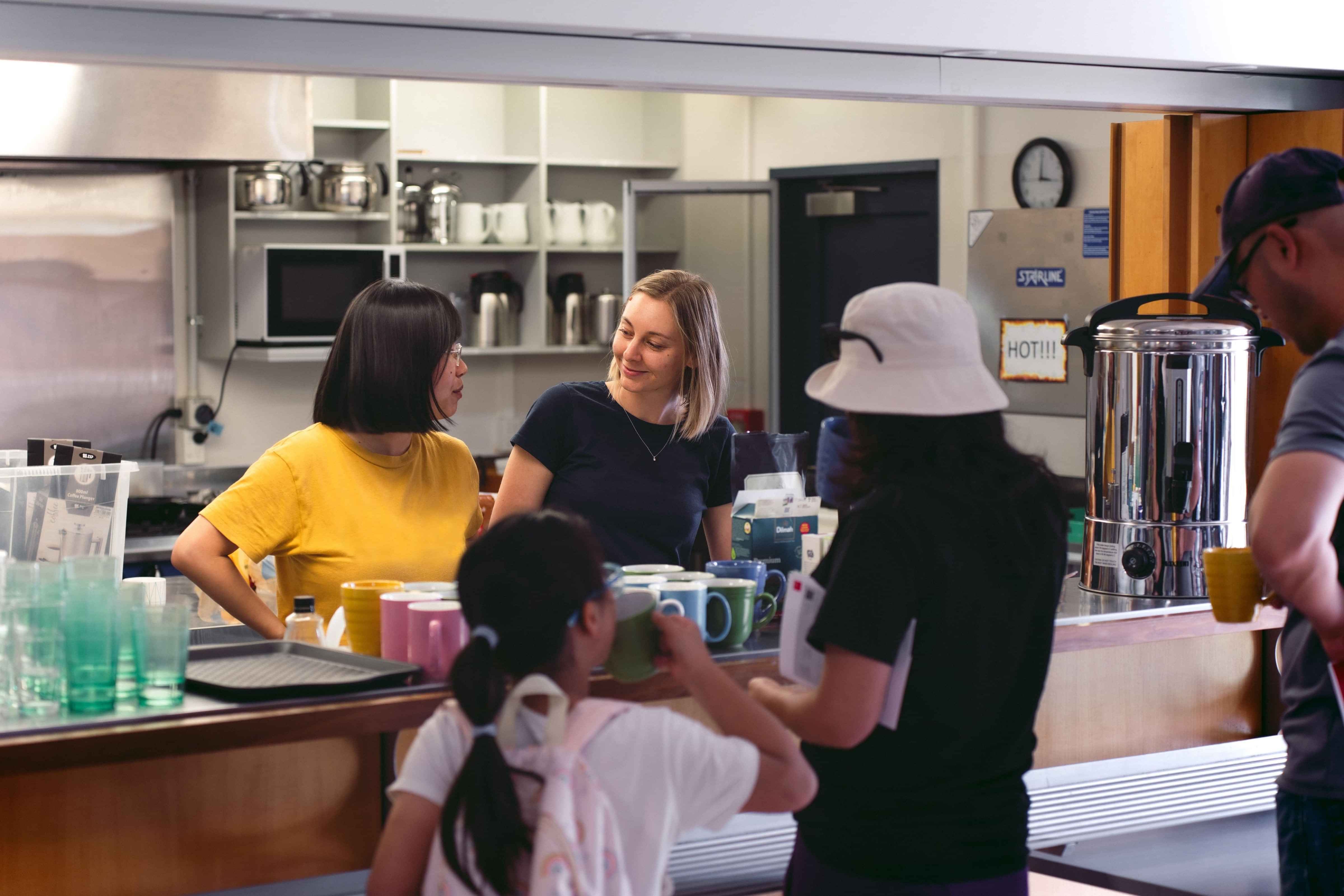 Two women serve hot drinks to a woman and a young girl after church