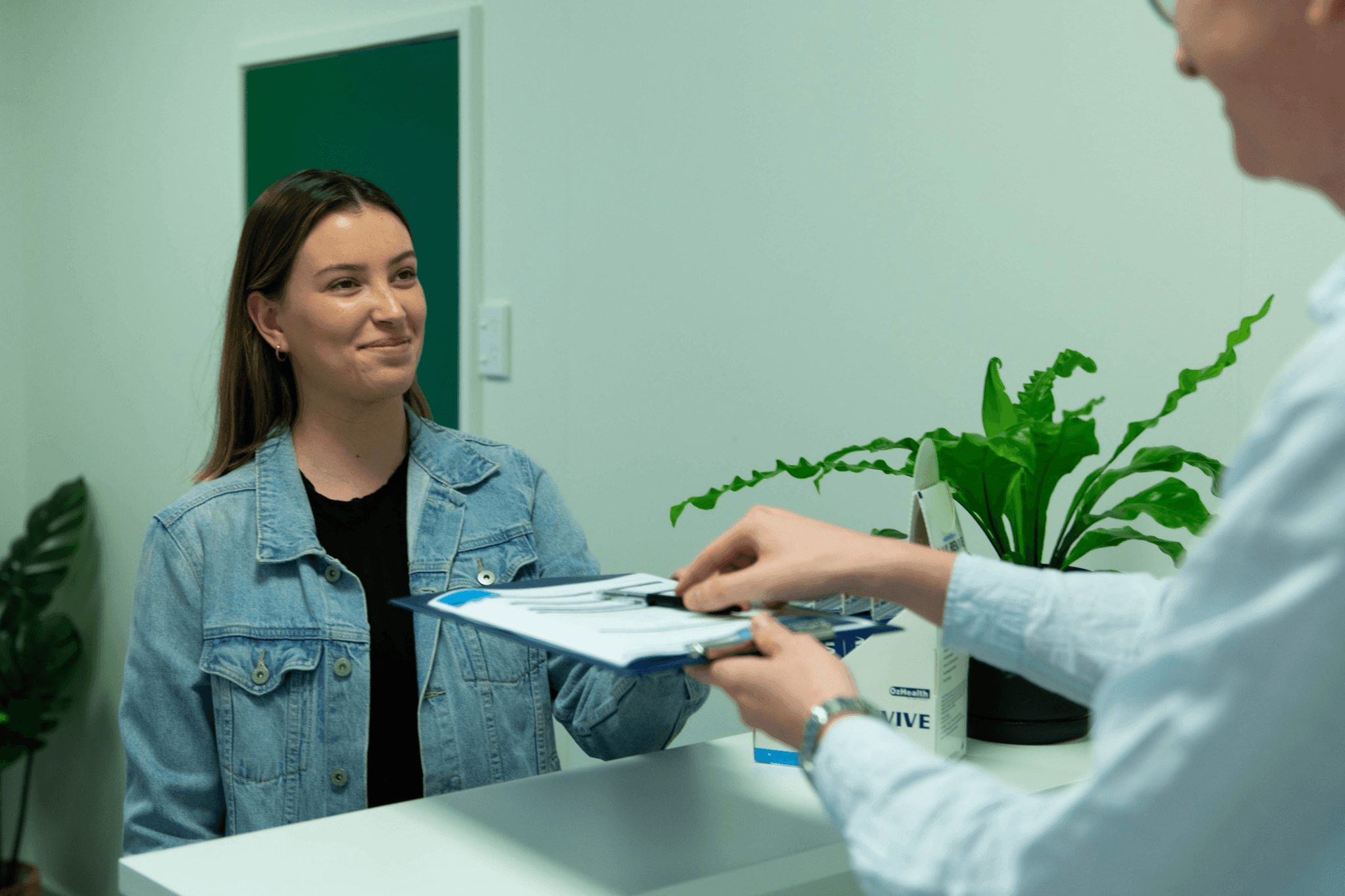 Patient handing a clipboard to receptionist at clinic desk.