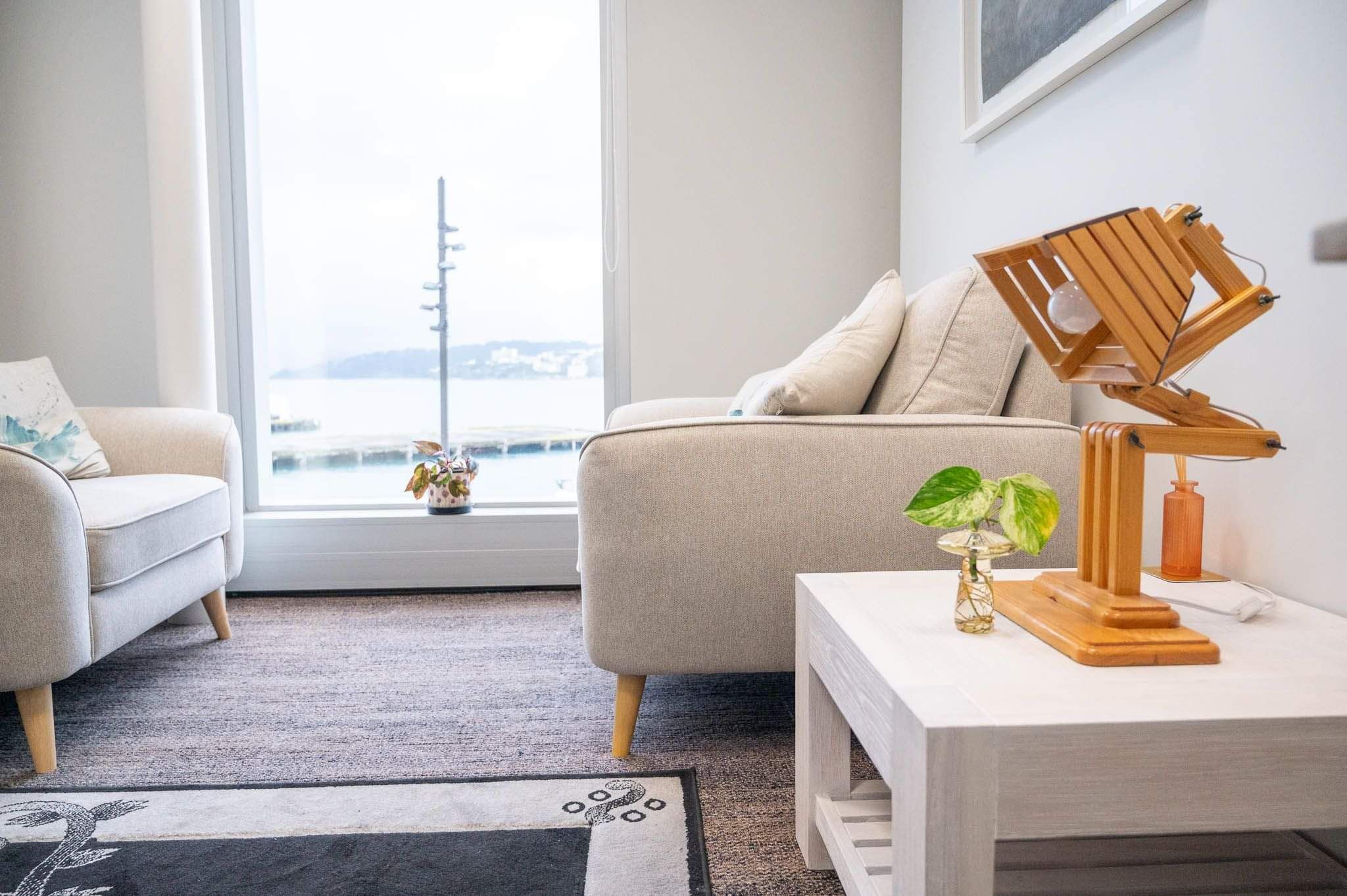Beige armchairs in an office with a wooden lamp and small plant on a white side table.