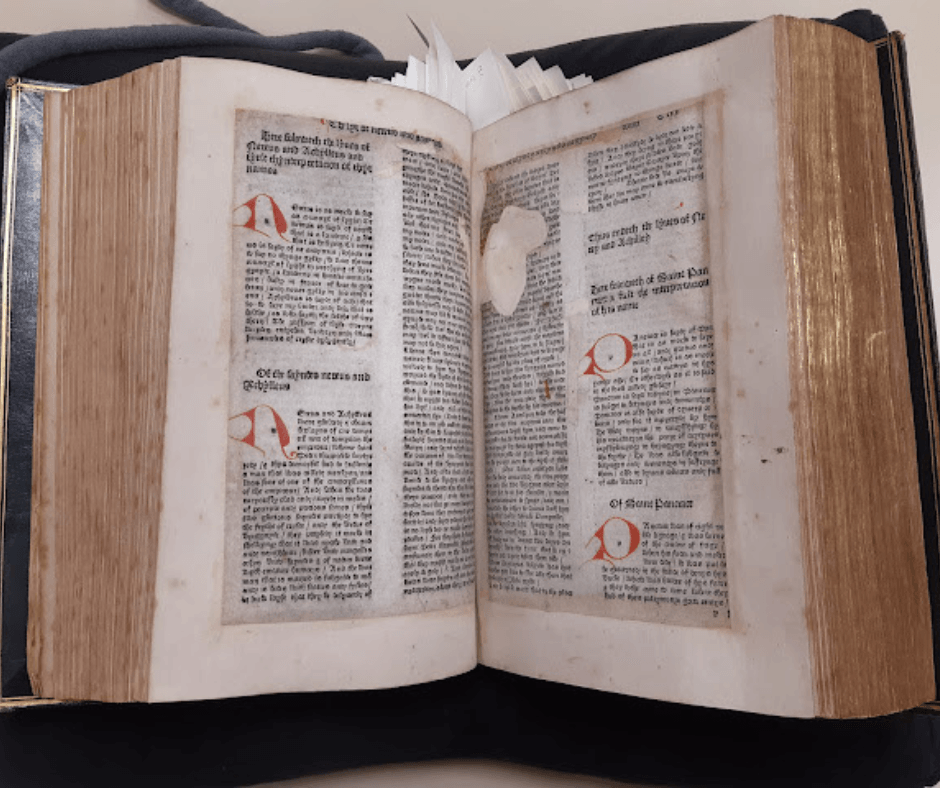 Fifteenth century book is open to display two pages. Black text with red initial letters. Some damage visible.