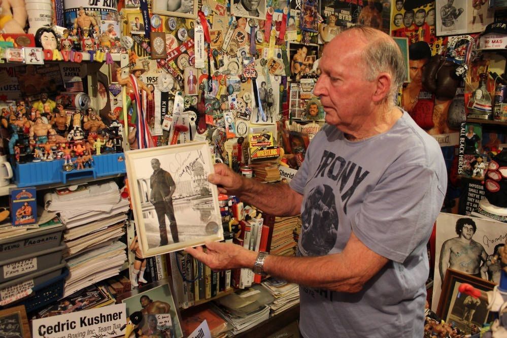 Dave in his room of memorabilia, holding a framed photo of a man.