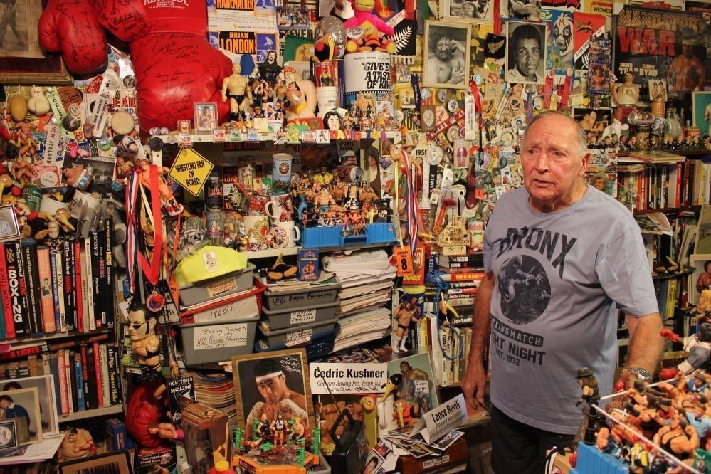 A man standing in a room that is full of boxing memorabilia - books, photos, medals, gloves, models, promotional and autographed items.