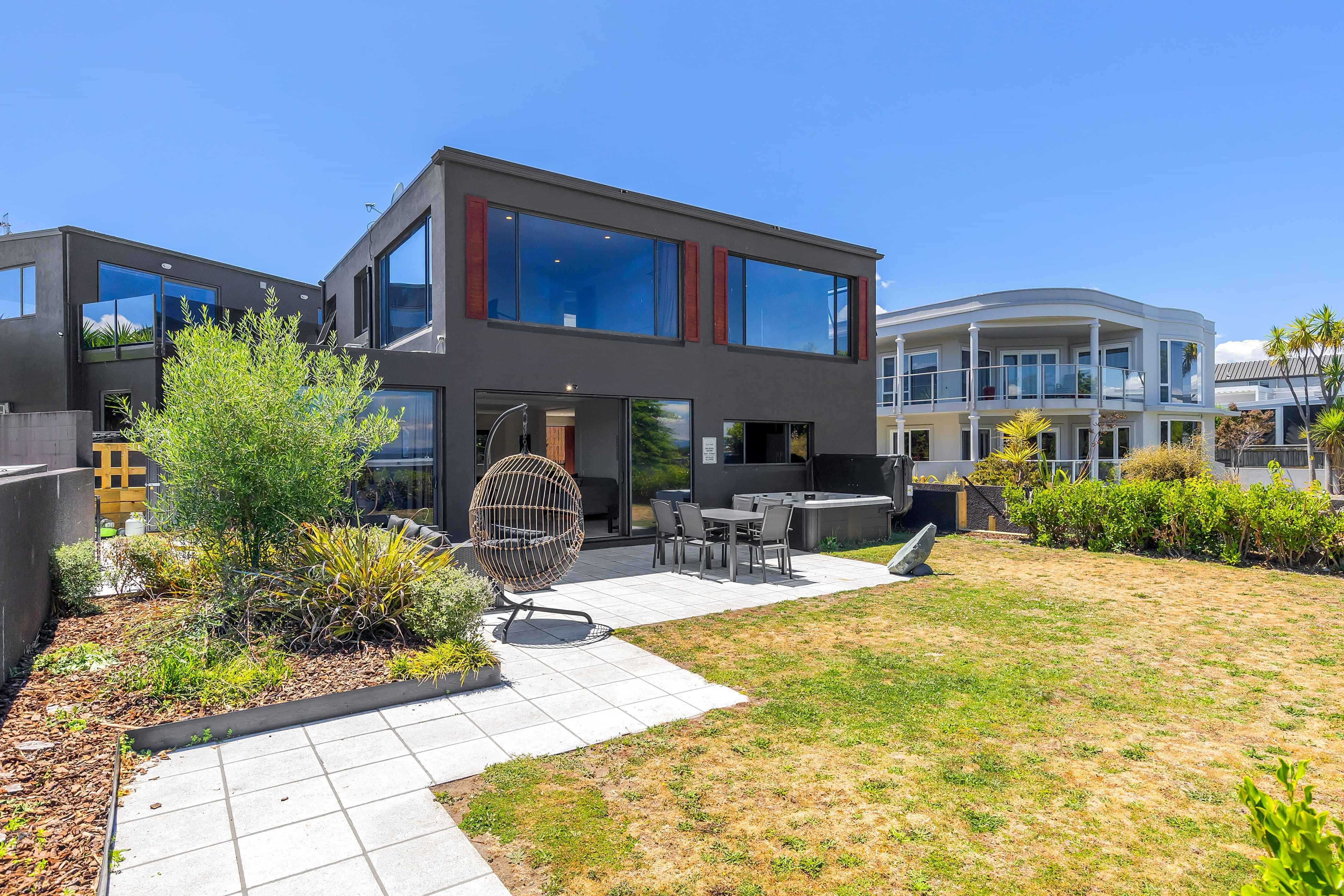 Modern black two-storey holiday home in Taupo with landscaped garden, hanging egg chair, and outdoor seating