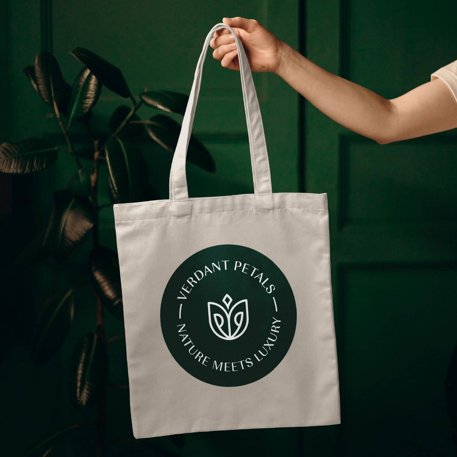 Hand holding a natural canvas tote bag with the circular Verdant Petals logo.