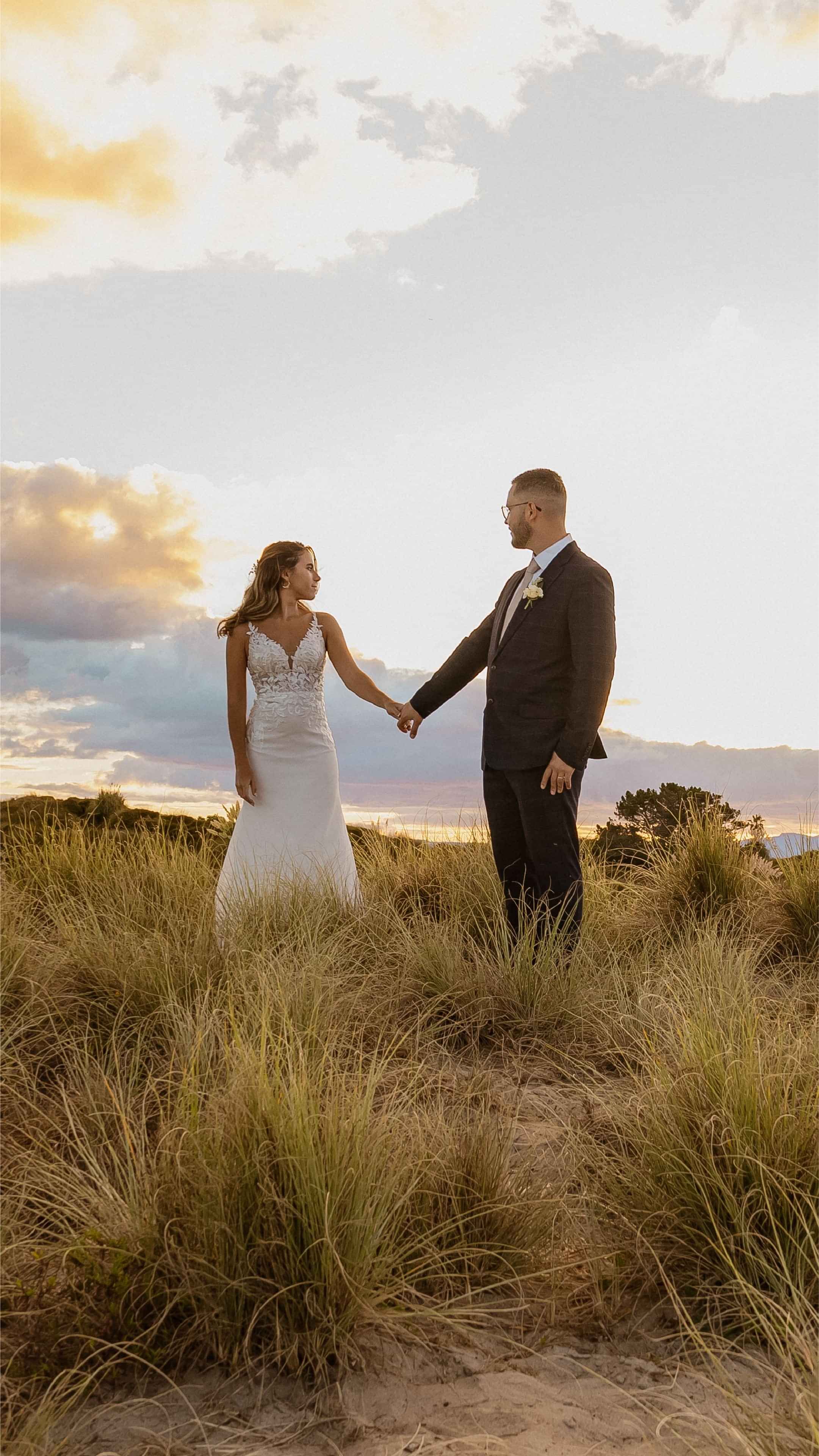 Bride and groom holding hands in a field at sunset, representing wedding photography.