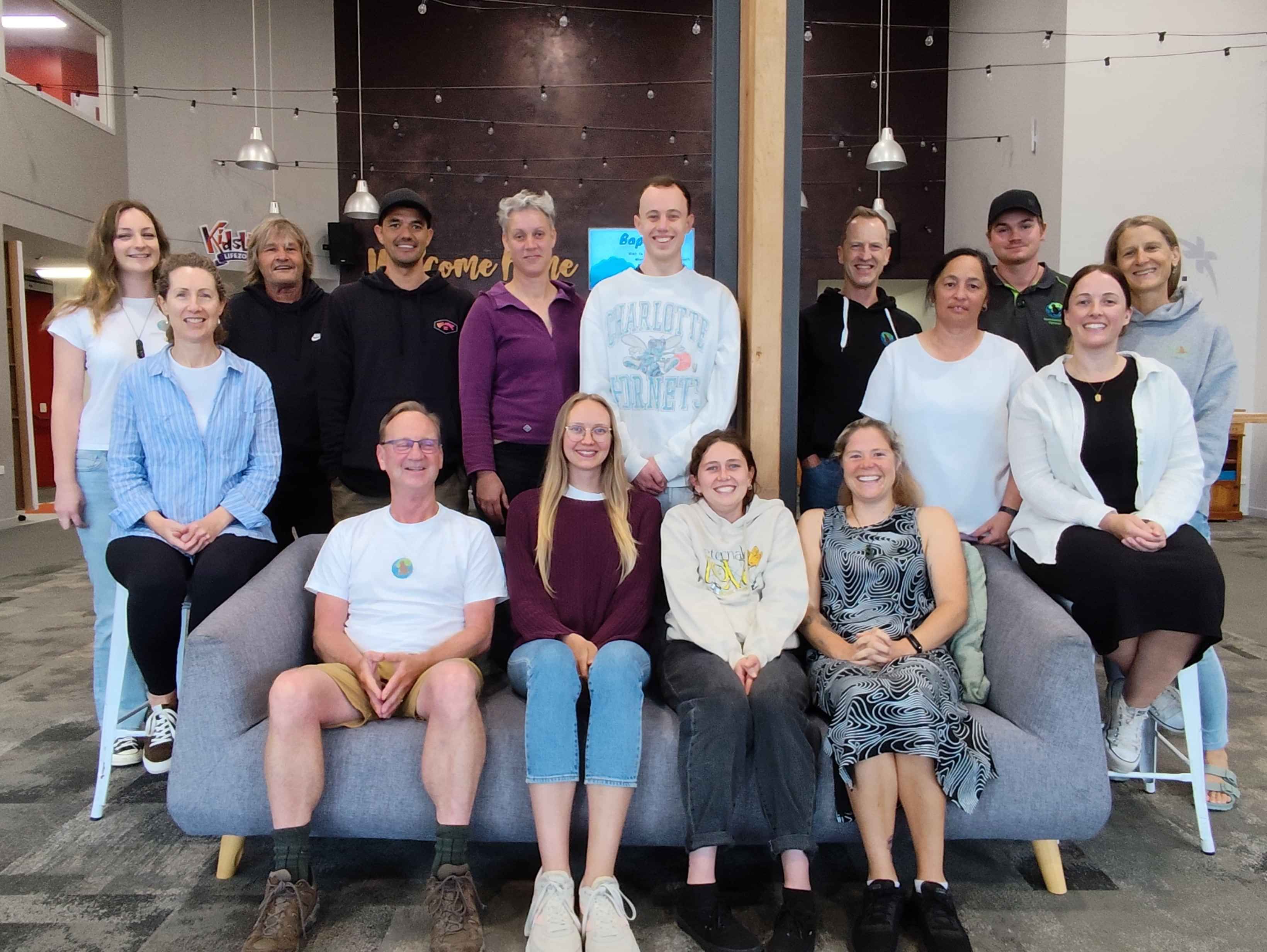 Team photo, a group of about 20 people some sitting on couches, some standing around all smiling for camera
