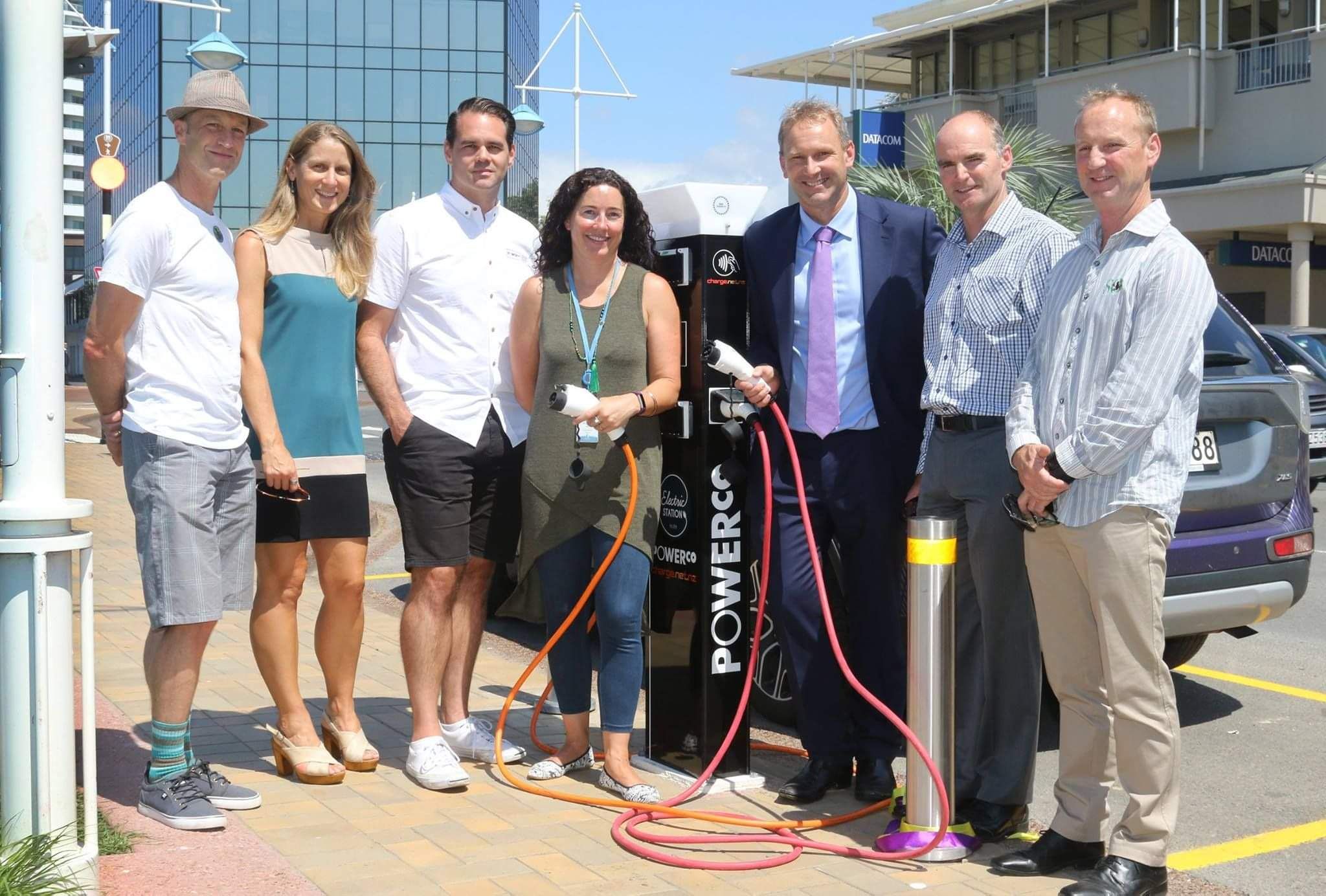 group of people standing next to electric vehicle charging station