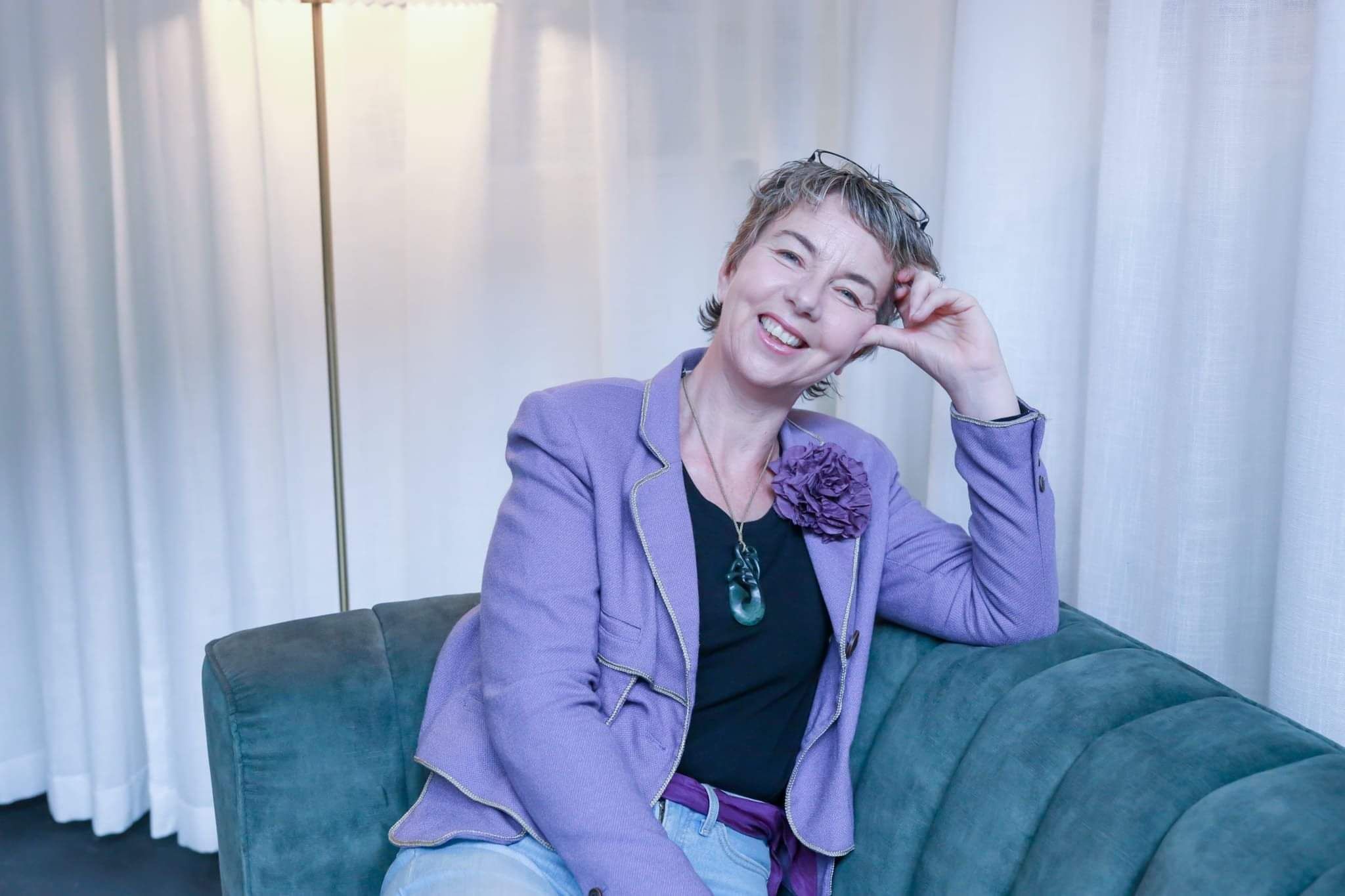 marketing strategist maree gately in a purple jacket on a green couch, smiliing