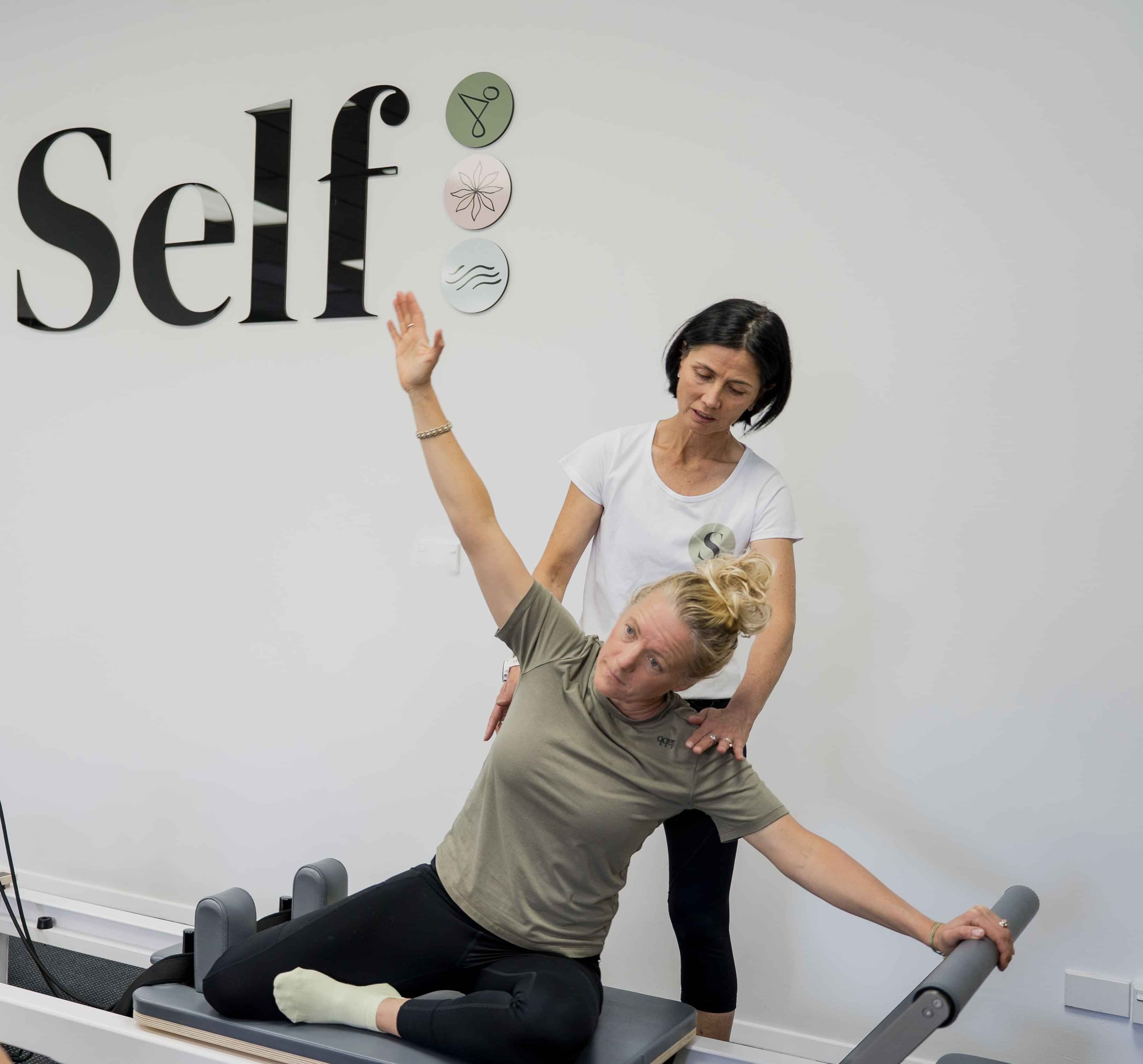 Image of instructor showing a woman how to do a Pilates exercise at Self, wellness studio in Alexandra.