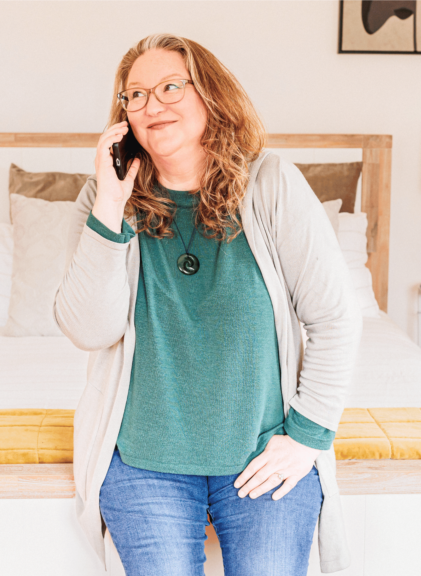 Photo of Leadership Coaching, Elizabeth, sitting on the edge of a bed, looking away from the camera while on the phone.