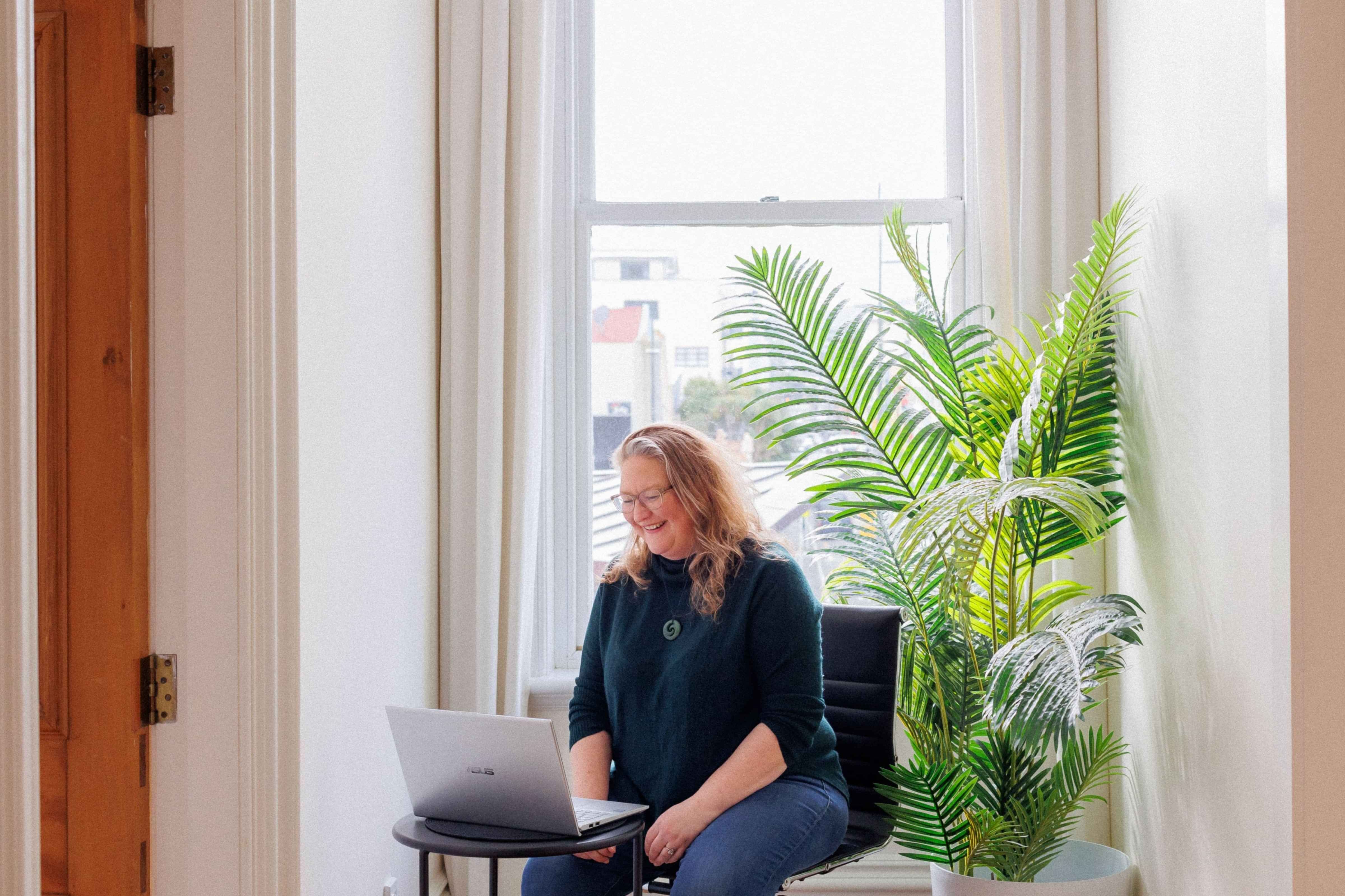 Photo of holistic health coaching expert, Elizabeth Marshall, laughing and looking down at a laptop.