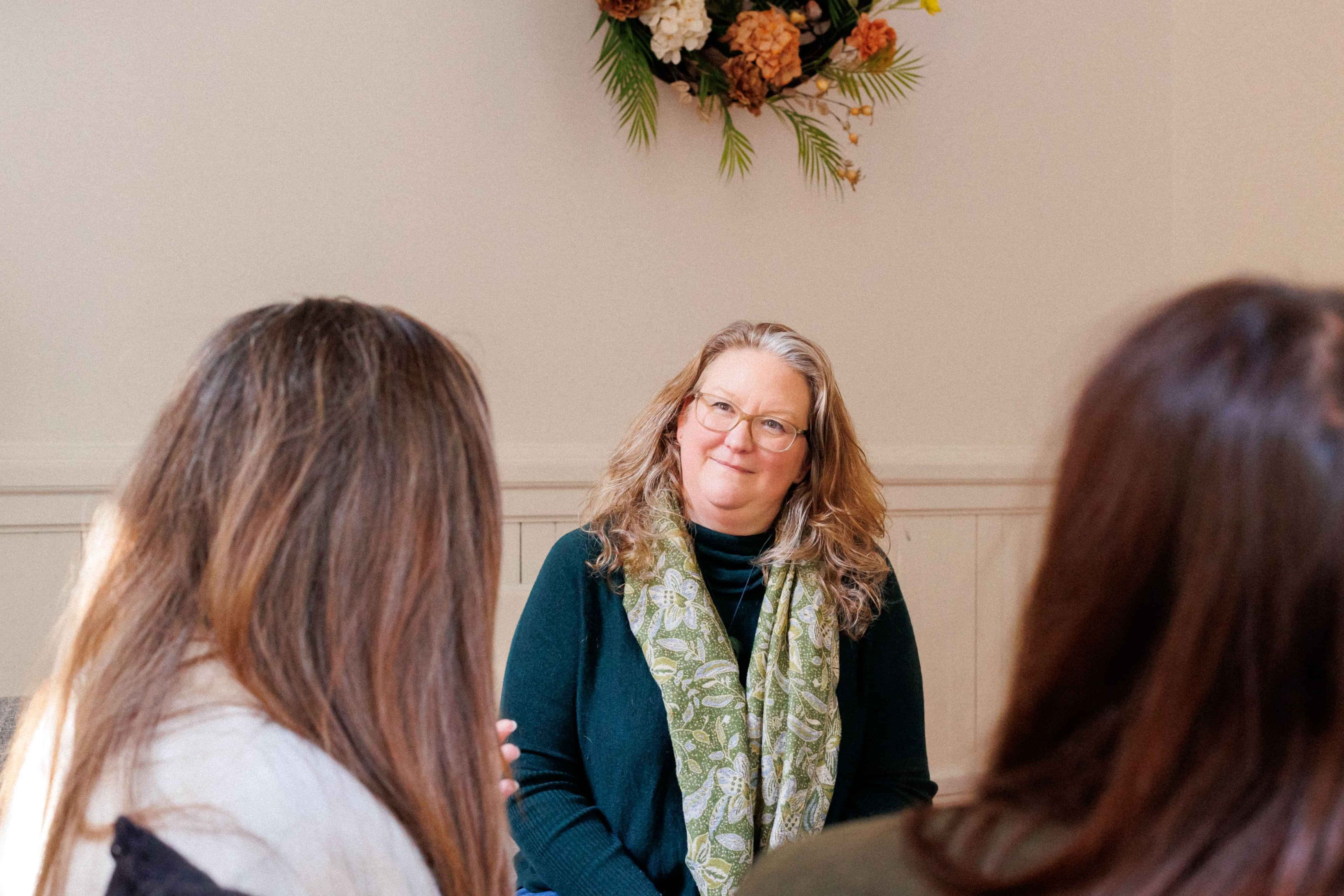 Photo of Elizabeth group coaching with two women. Elizabeth is facing the camera and two women with their backs to the camera.