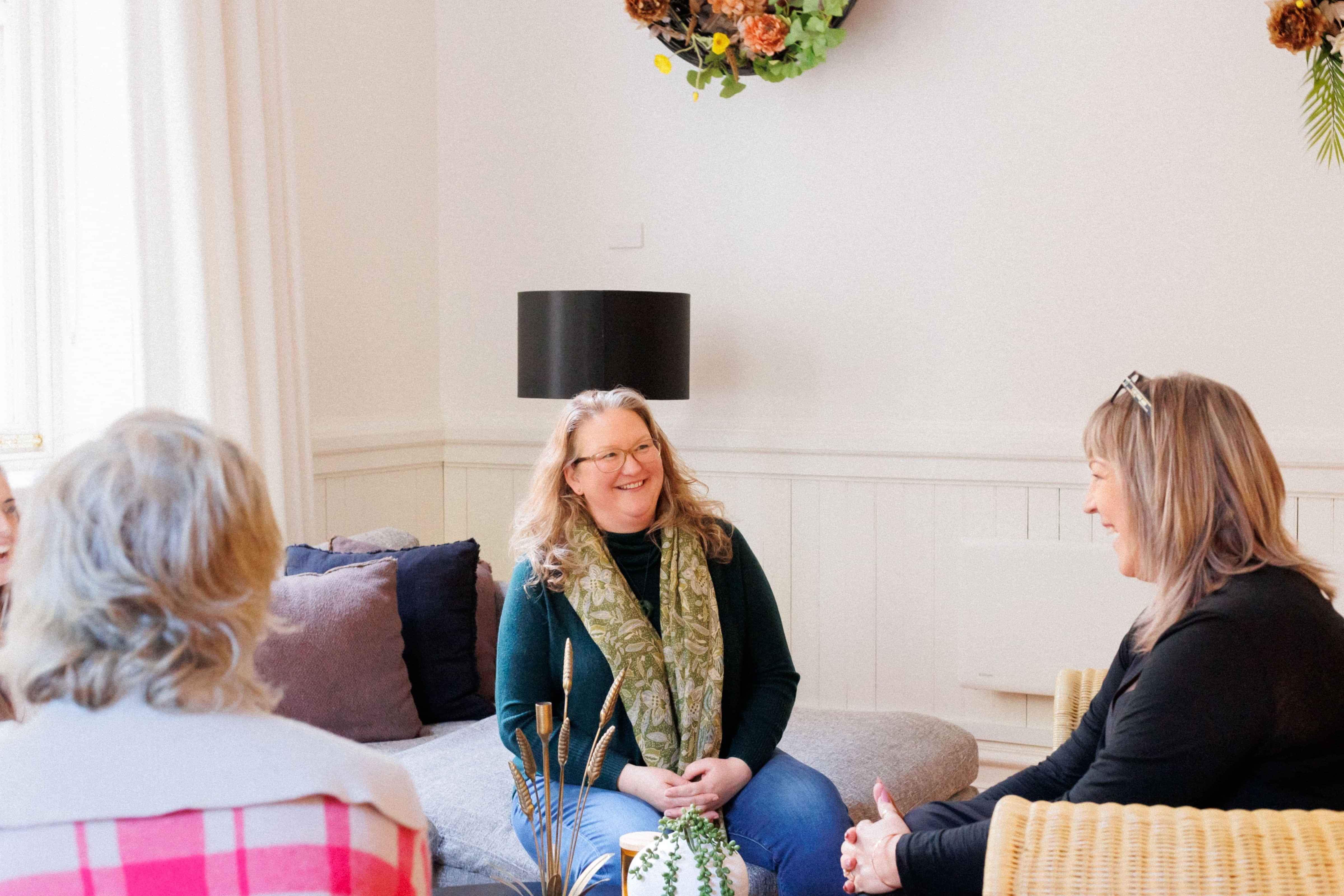 Photo of Elizabeth group coaching with two women. Elizabeth is facing one of the women smiling and two women with their backs to the camera.