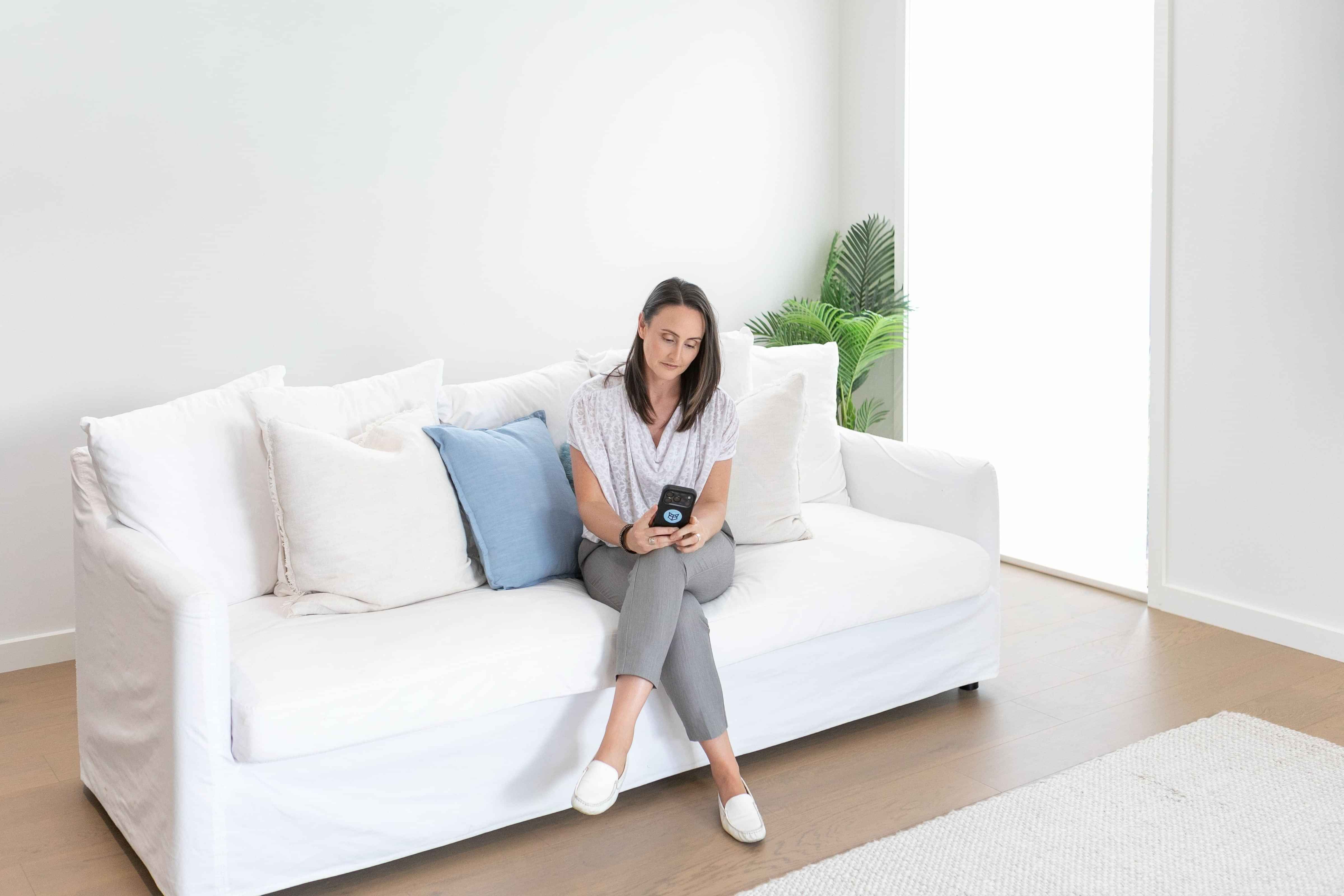 Zoe Shepherd, Virtual Assistant looking at phone seated on a white couch
