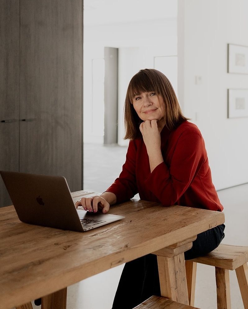 Sacha Adair, founder of The Tribe sitting at a desk with her laptop.