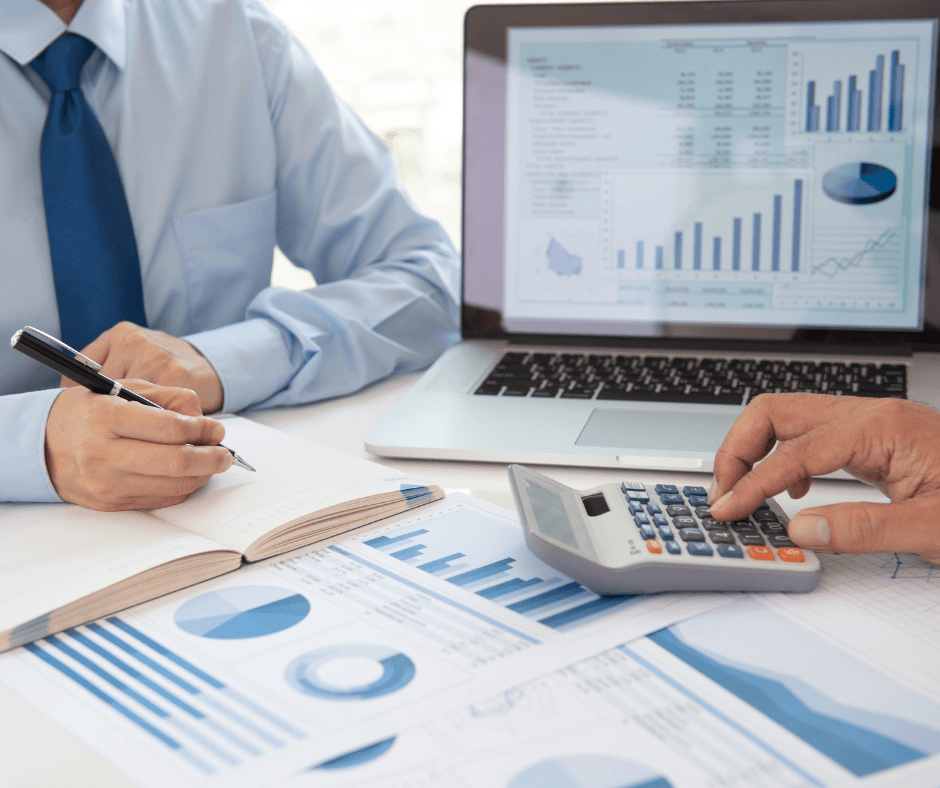 Laptop with Post-it note stating Tax Deadline and lots of paperwork lying around it, showing numbers and reports. Pencil and notepad.