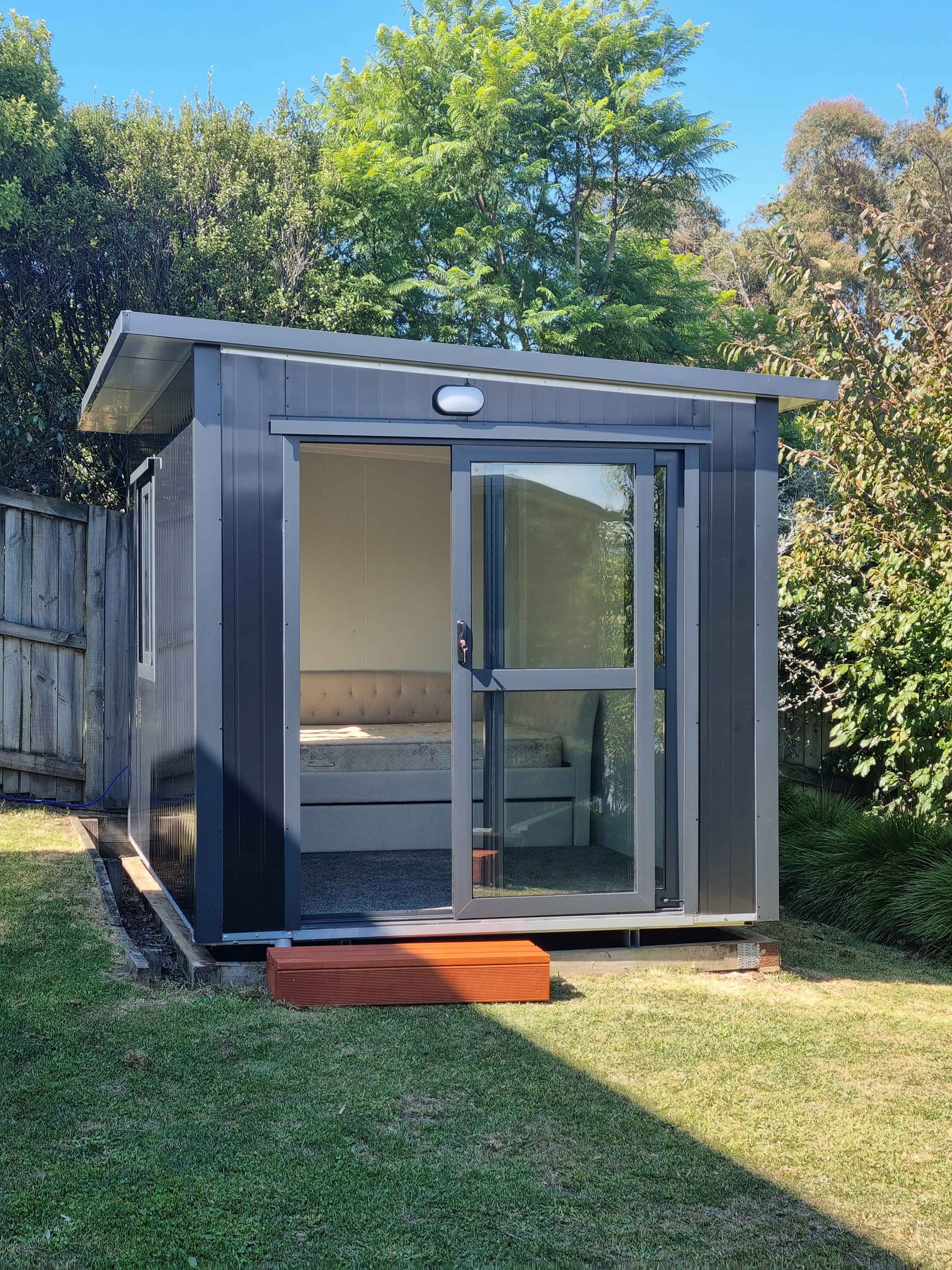 3.6m x 2.4m black cabin with two windows and entrance step