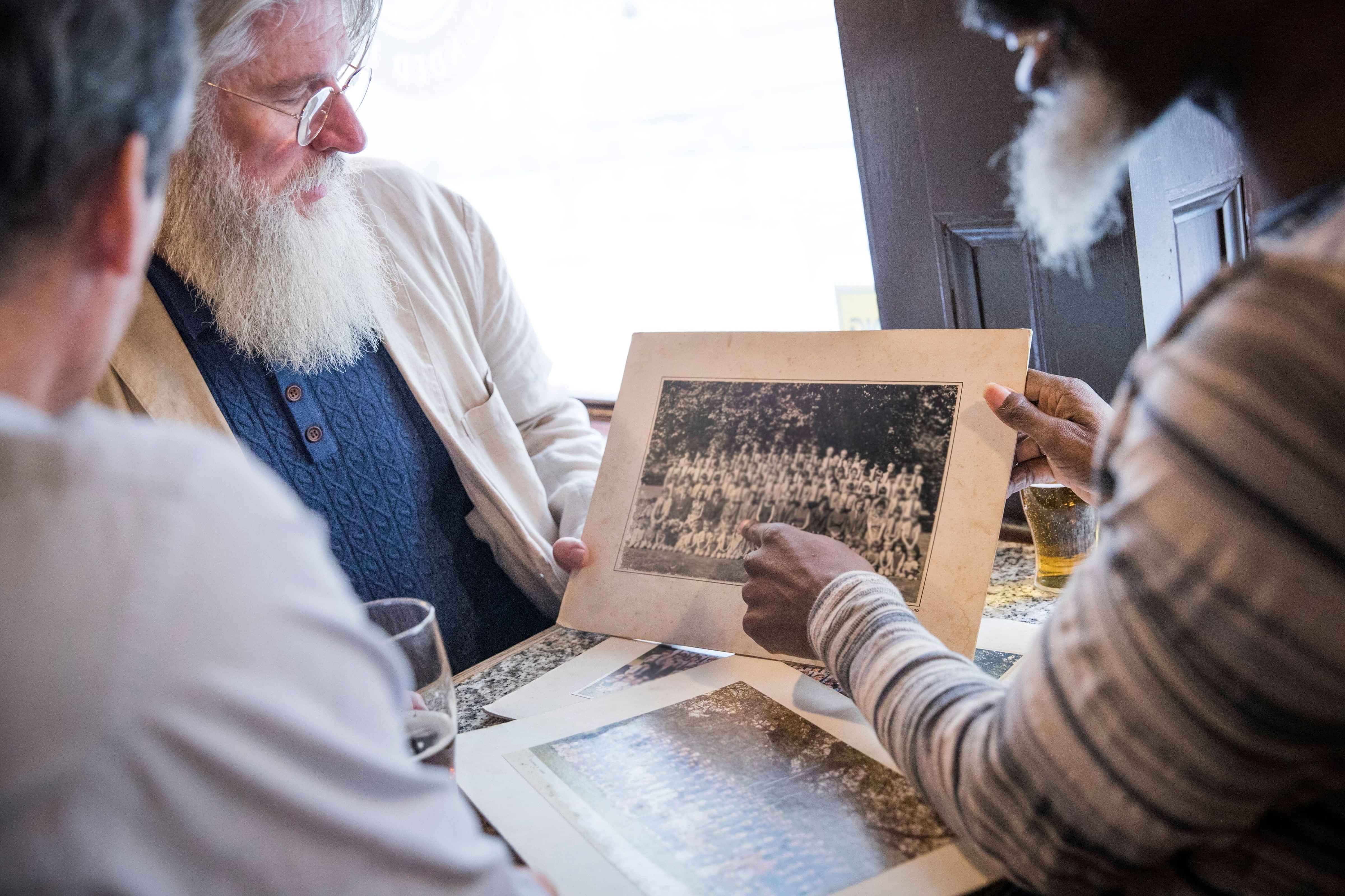 Three people discussing a photo of a large group of people