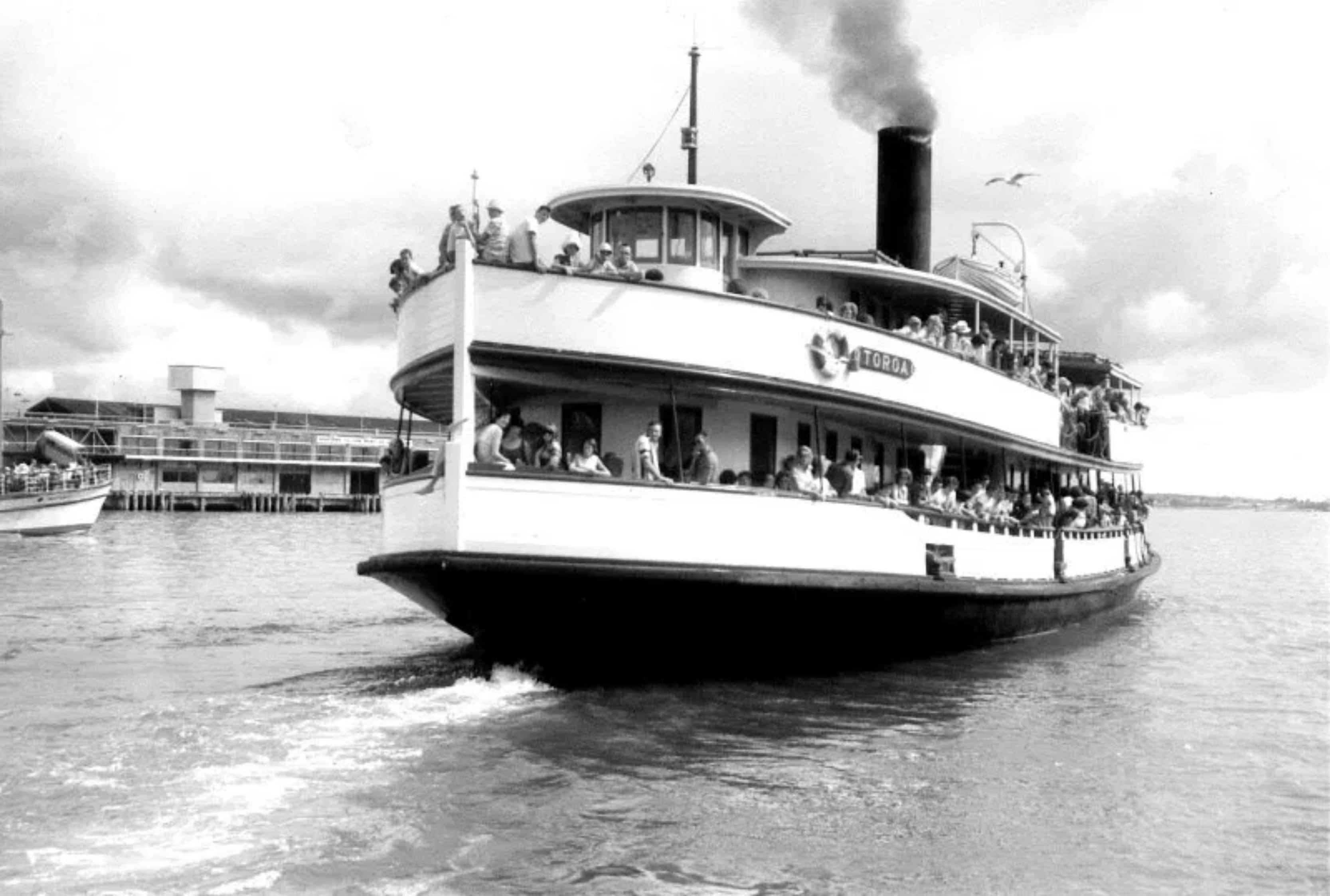 An old steam boat on the water with crowds of people standing on the balconies