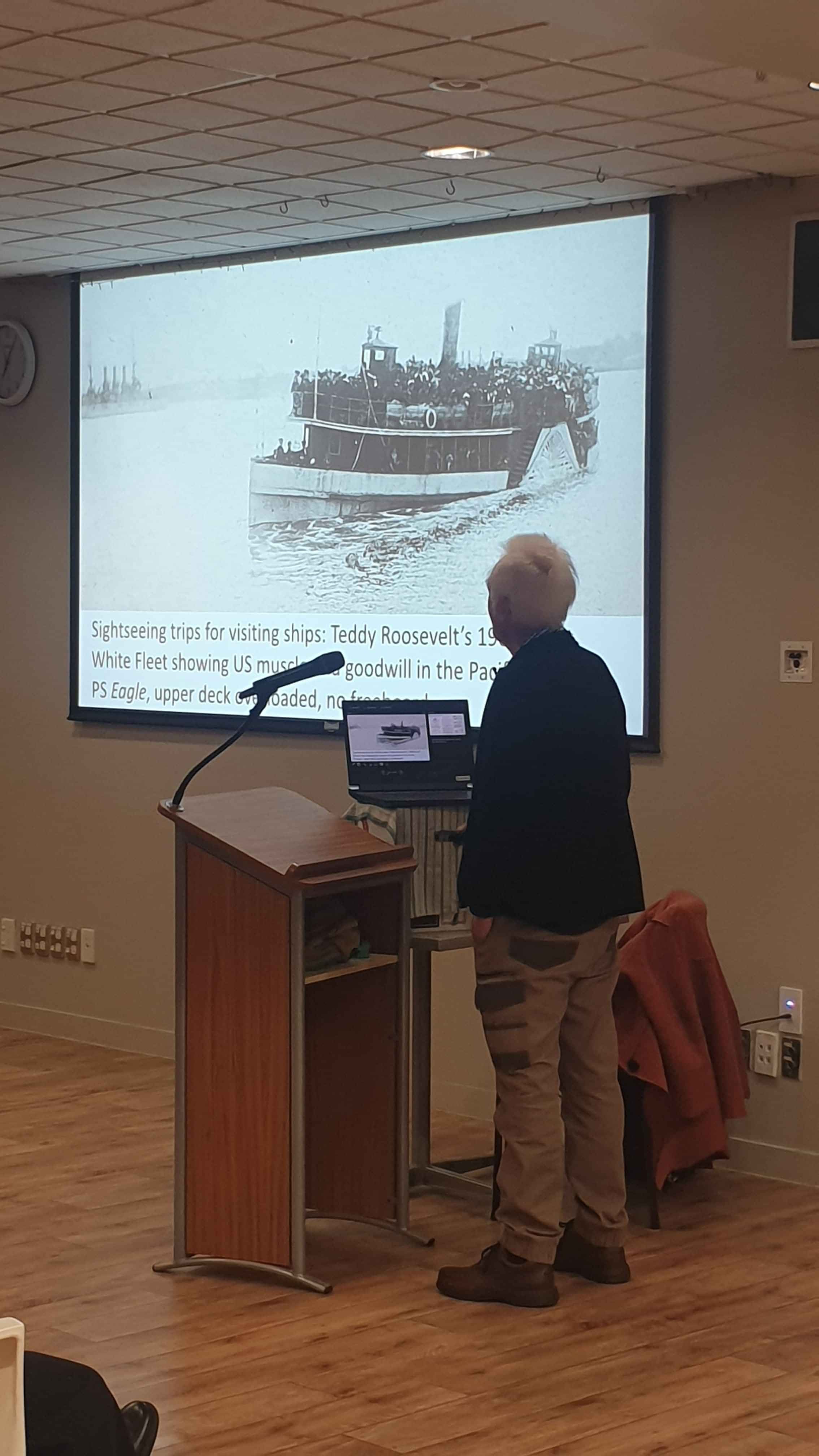 Male guest speaker at a podium with his presentation projected on the wall
