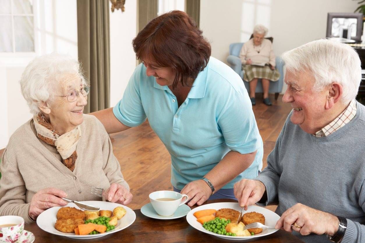 Caregiver checking on aged residents eating their main meal