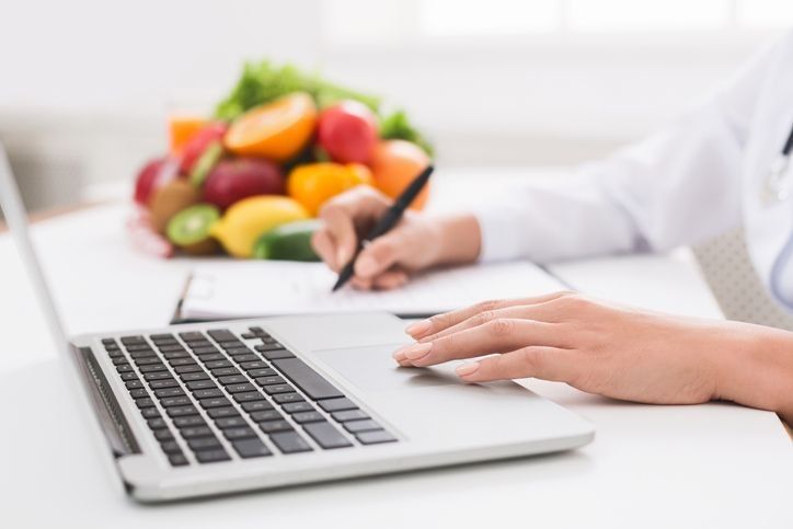 A person (hands only) working on their computer and taking notes with fruit in the background