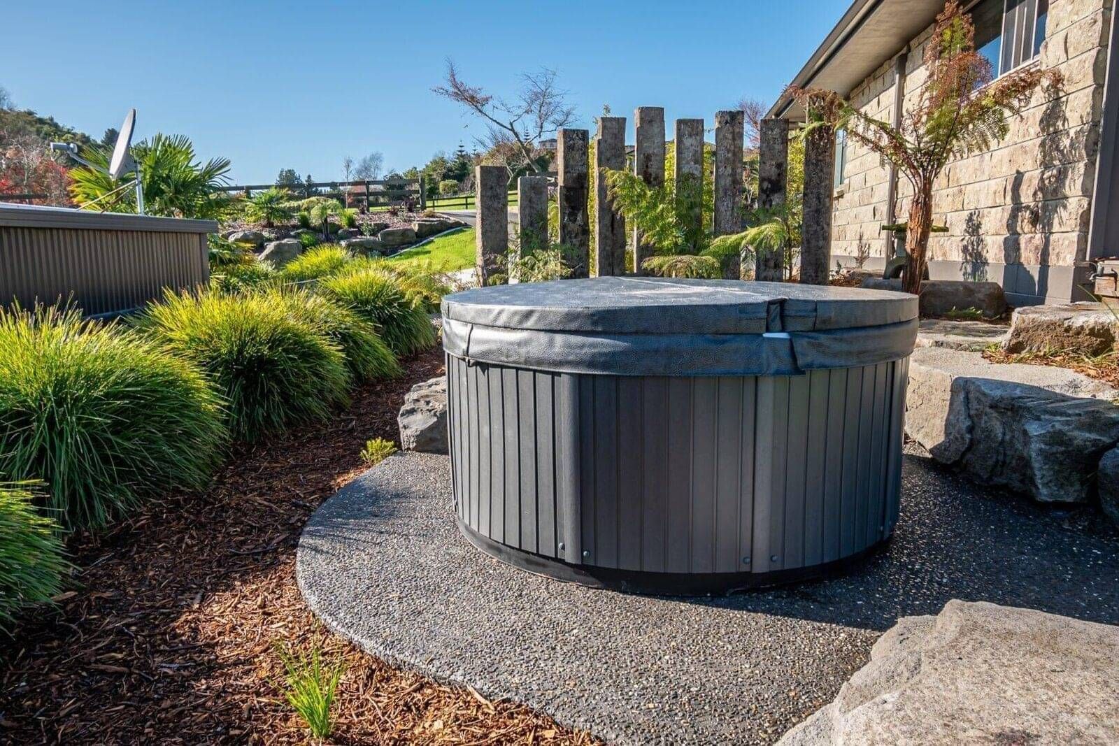 Landscape design in Rotorua featuring landscaped area designed for a spa pool with natural stone, native plants and wooden columns as a feature