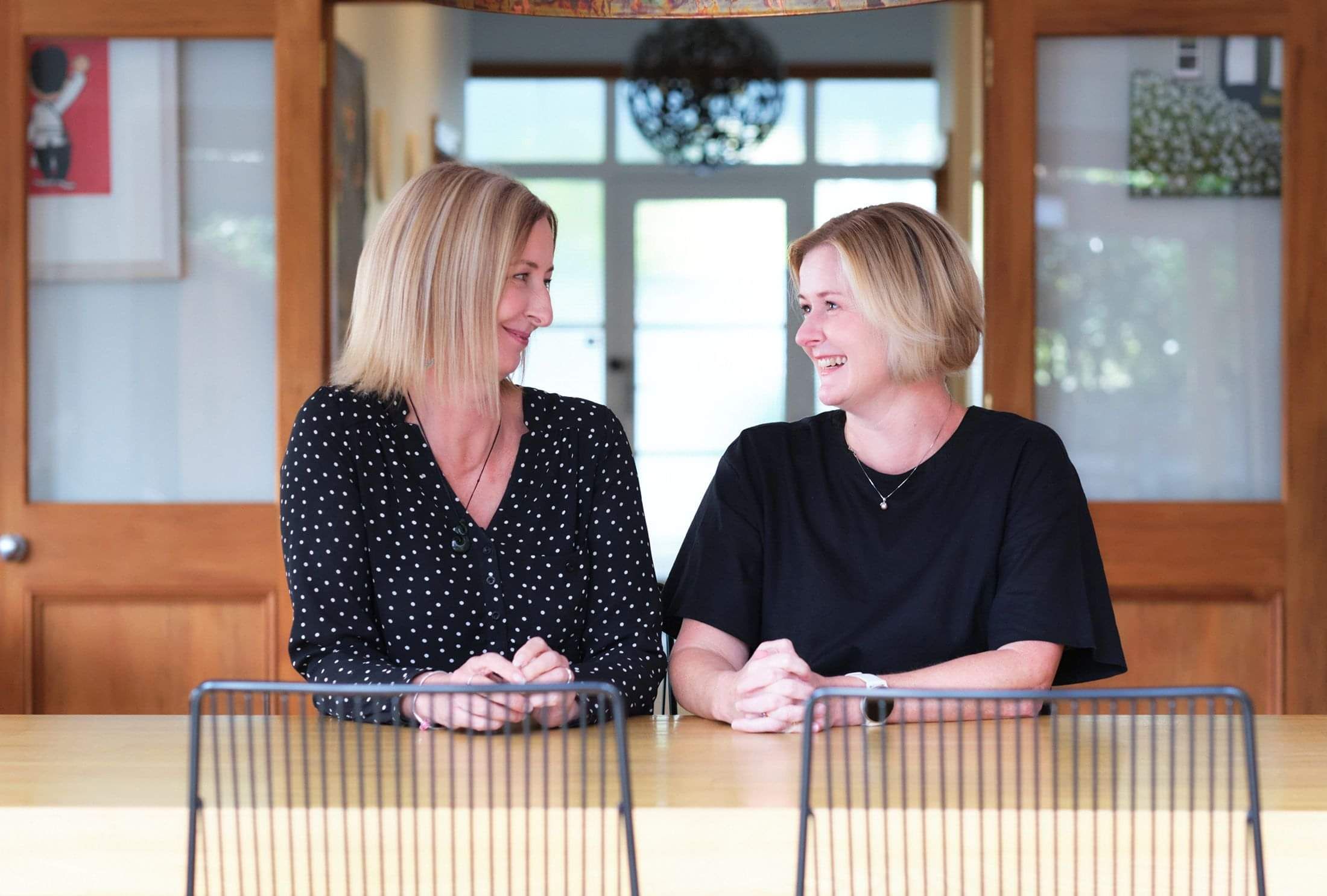 Photo of Gabrielle Ralph and Claire Turner from Two Little Birds Consulting sitting at a table smiling at each other