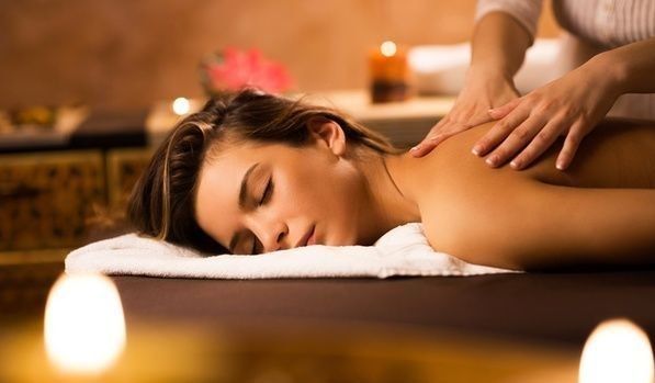 Picture of a lady lying face down on the massage table with her head facing out and the massage therapist hands on her back massaging.