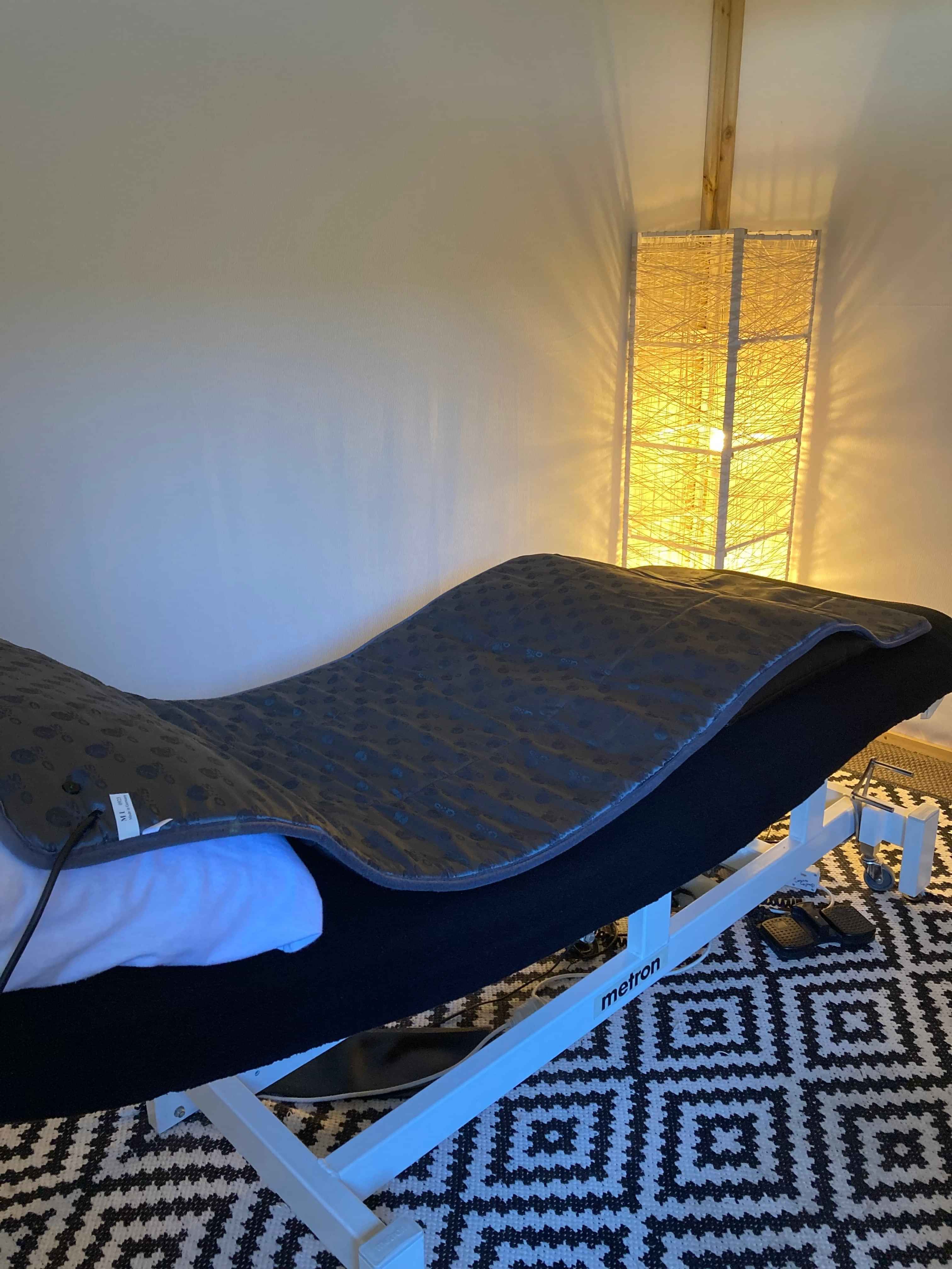 Picture of the QRS Mat lying on top of the massage bed with a large white and yellow light in the corner of the room
