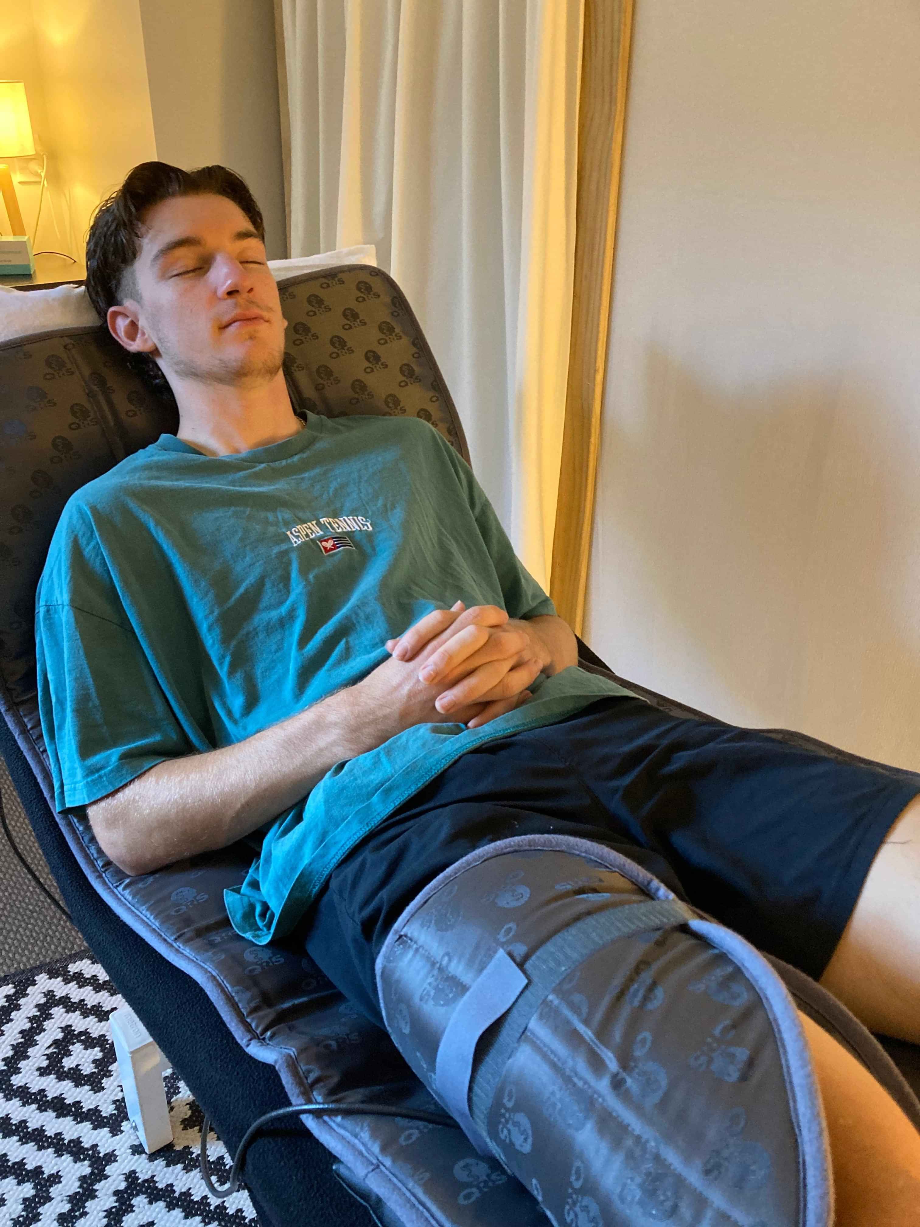 Picture of a young man lying on top of the PEMF Mat and using the pillow applicator on his quads for targeted treatment