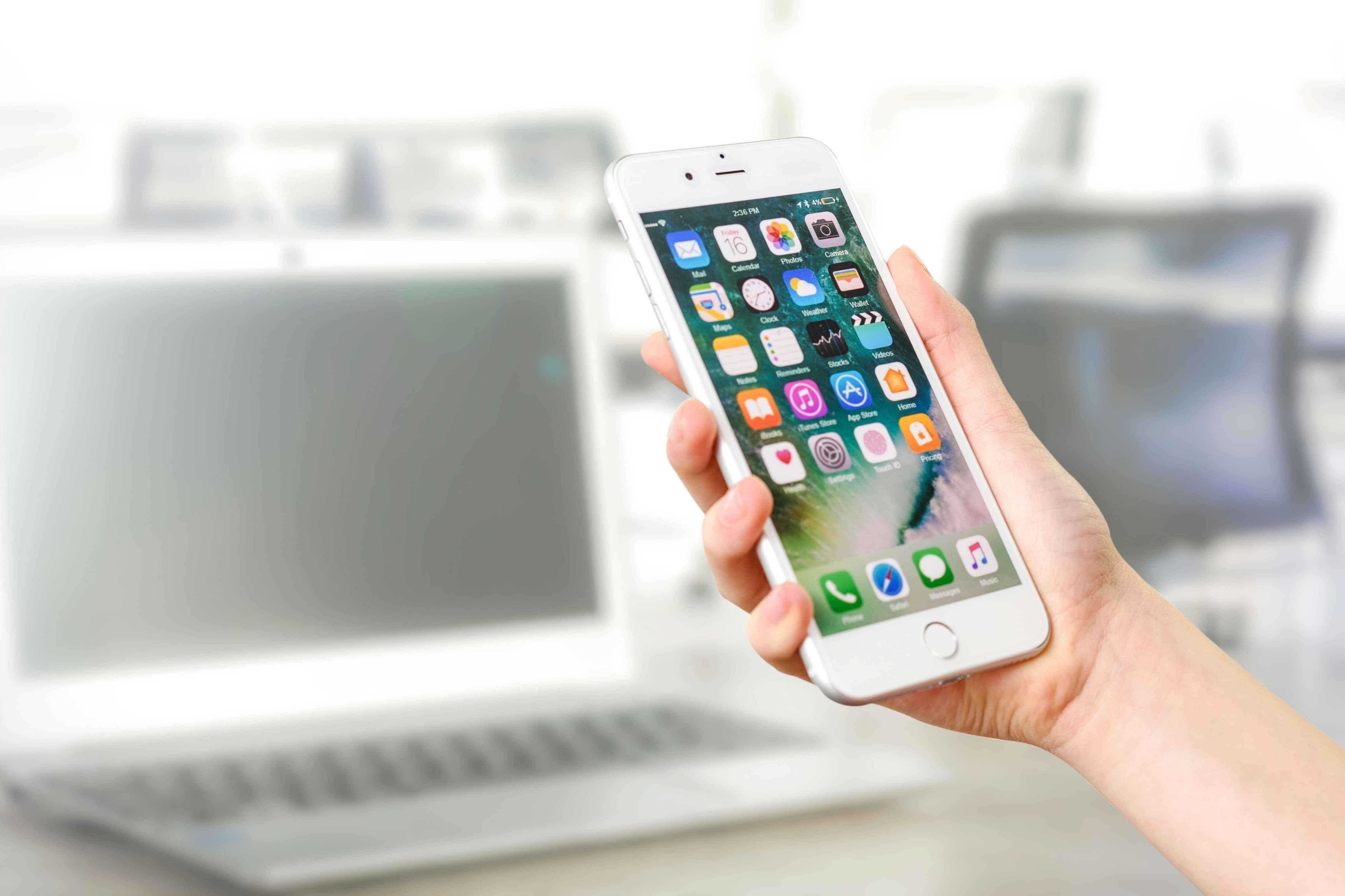 Picture of someone holding a phone with a laptop blurred in the background