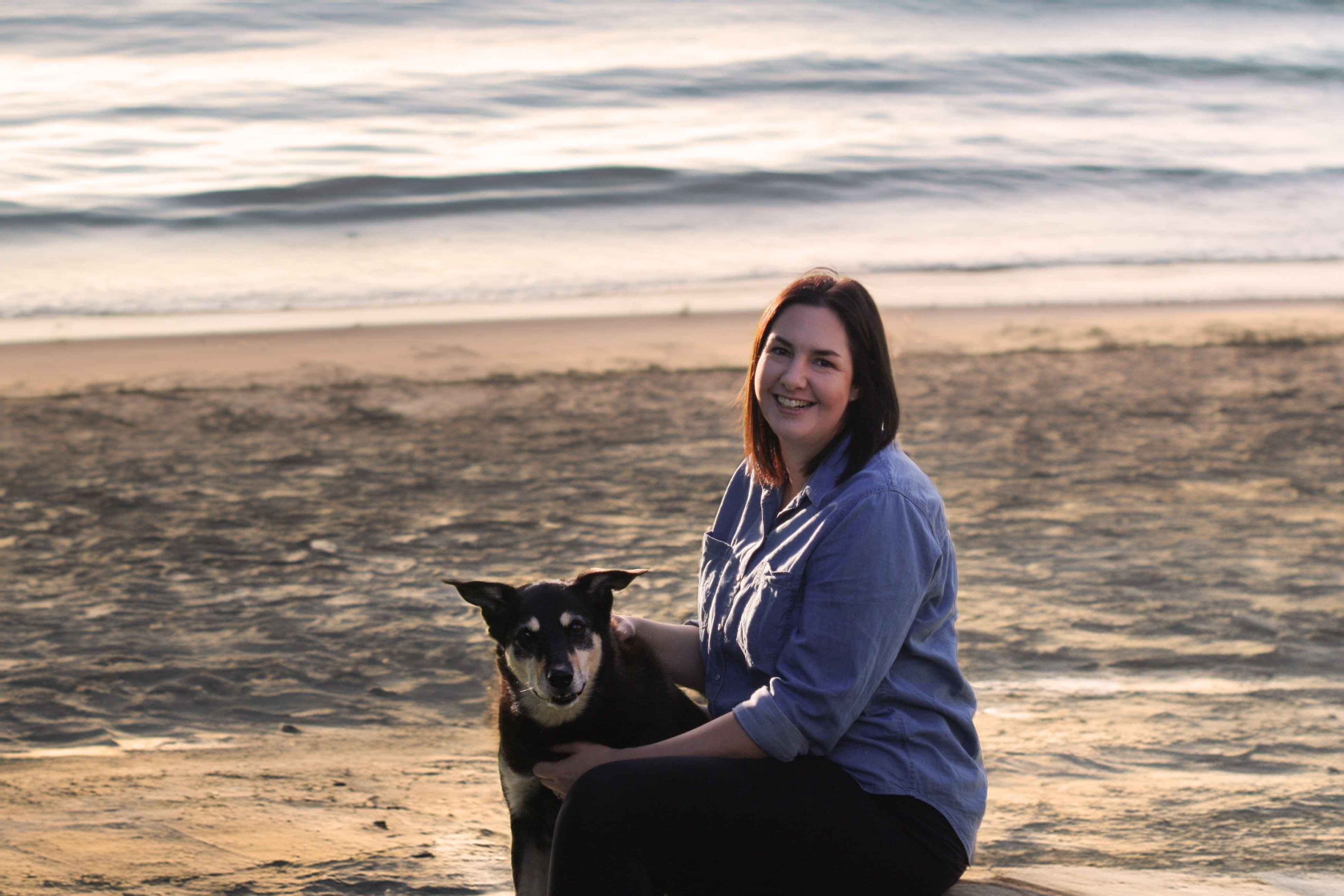 A female and a black and tan dog on the beach at dusk