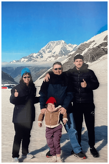 Family standing on snow beside a helicopter with snow-covered mountains in the South Island of New Zealand in the background.