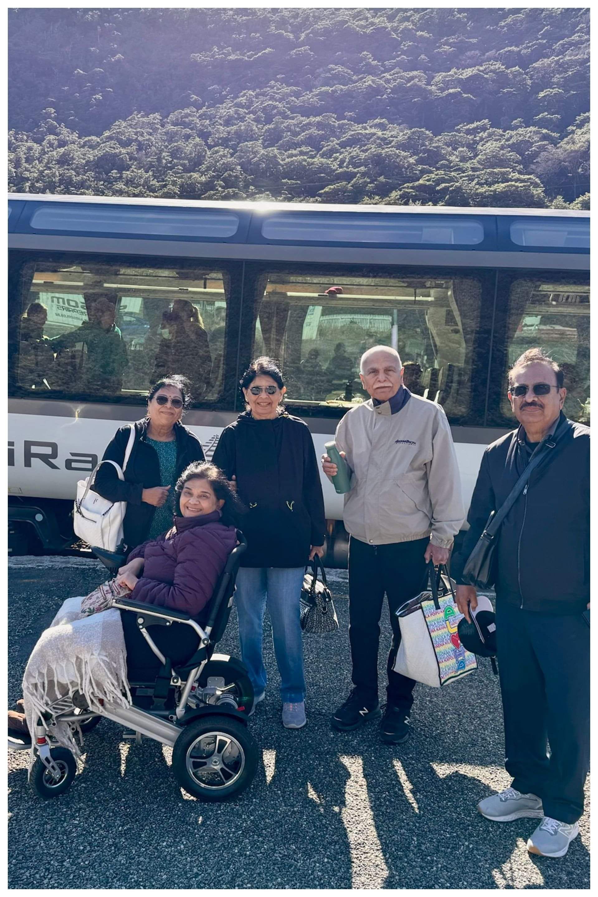 Family standing beside a KiwiRail train, with a woman in a wheelchair, showcasing accessible transport options for New Zealand holidays